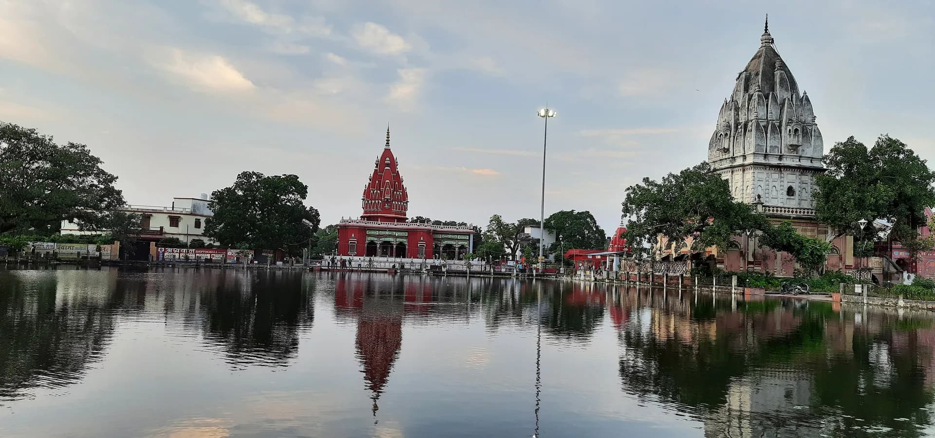 दरभंगा का शांत मंदिर तालाब, जिसमें बादलों भरे आसमान के नीचे लाल श्यामा माई मंदिर और सफ़ेद शिखर वाला मंदिर झलक रहे हैं