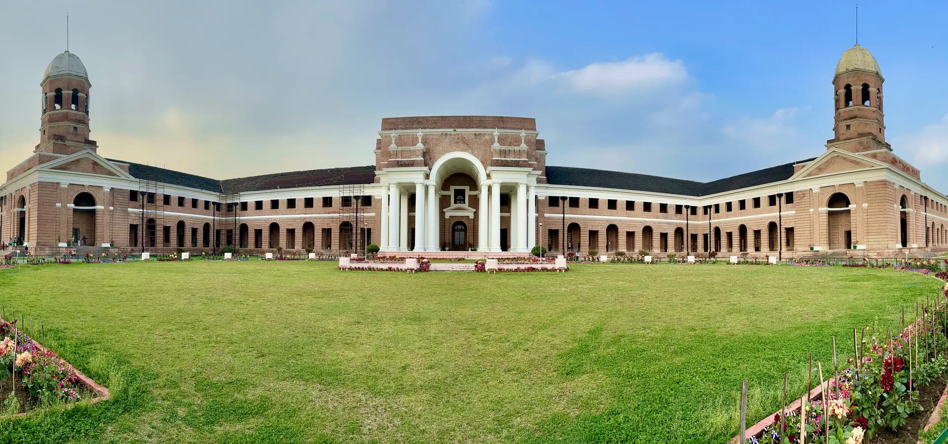 Panorama do Forest Research Institute de tijolos vermelhos, com torres gêmeas e entrada com colunas atrás de um gramado verde