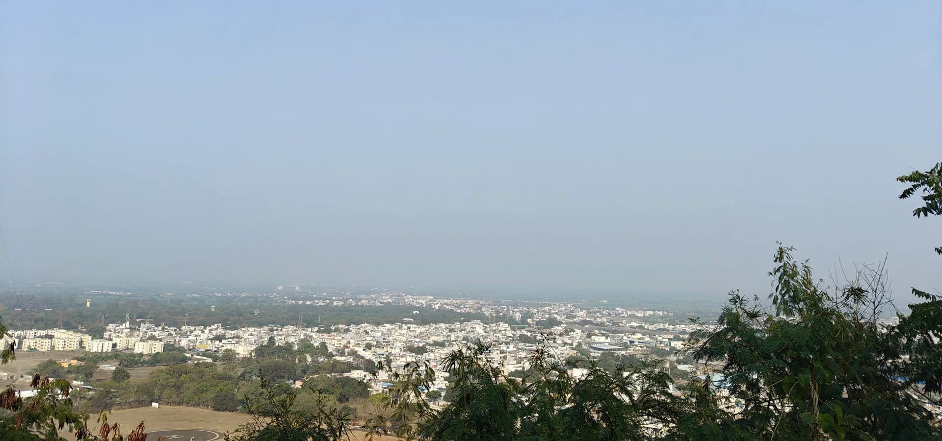View from Tekri hill over white rooftops of Dewas spreading across the flat Malwa plain under a pale blue sky