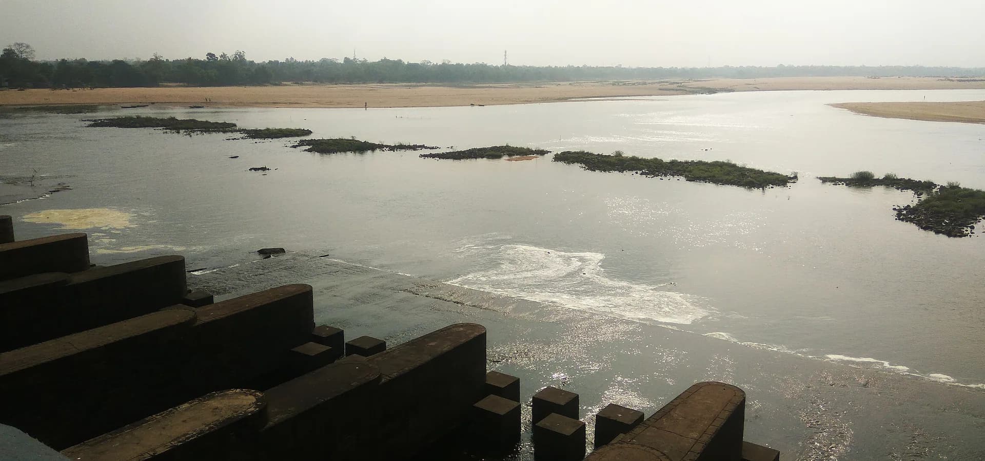 El ancho río Damodar con islotes verdes y bancos de arena visto desde los pilares de concreto de la presa de Durgapur
