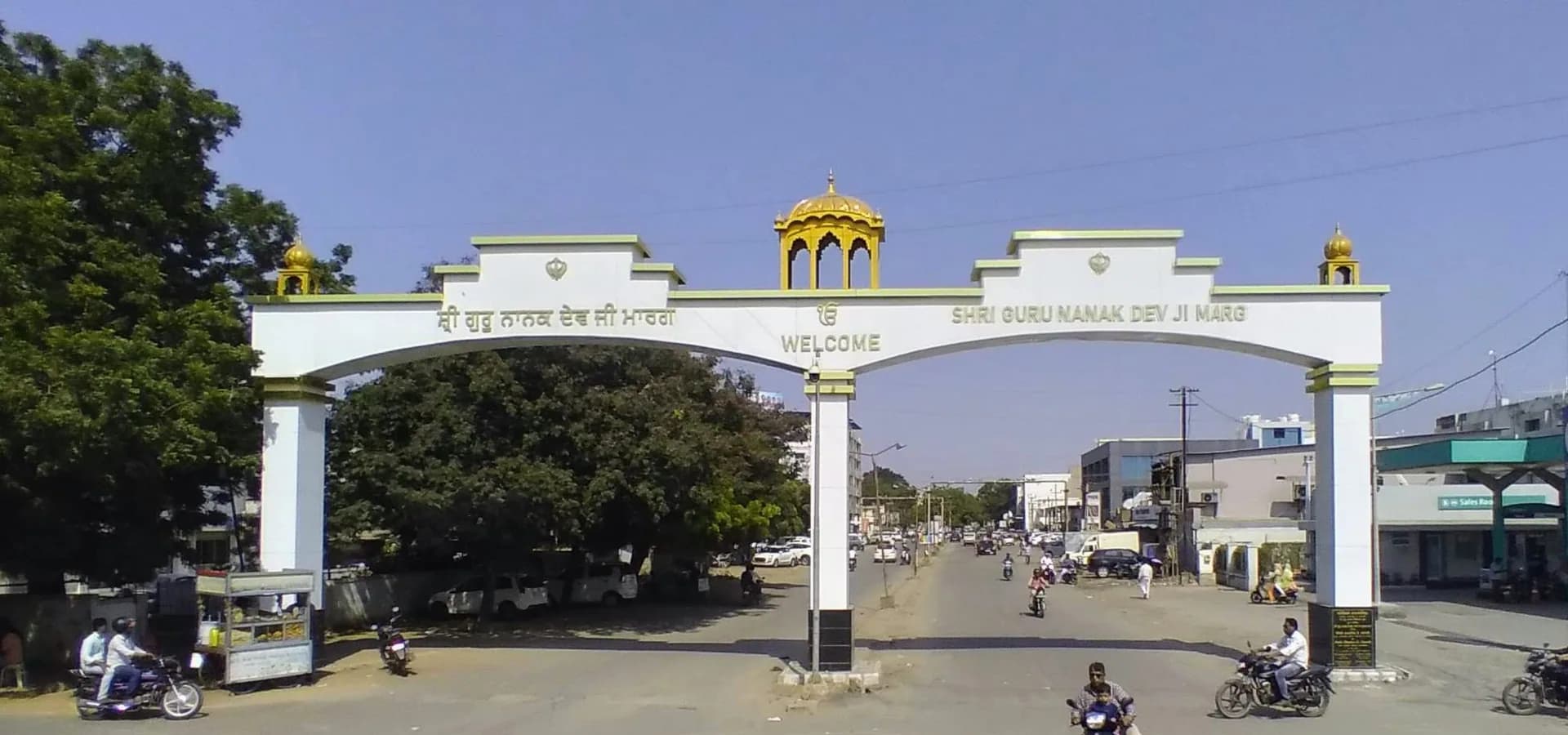 Weißer Bogen mit goldenen Kuppeln über der Shri Guru Nanak Dev Ji Marg in Ward 12B, Gandhidham, unter blauem Himmel