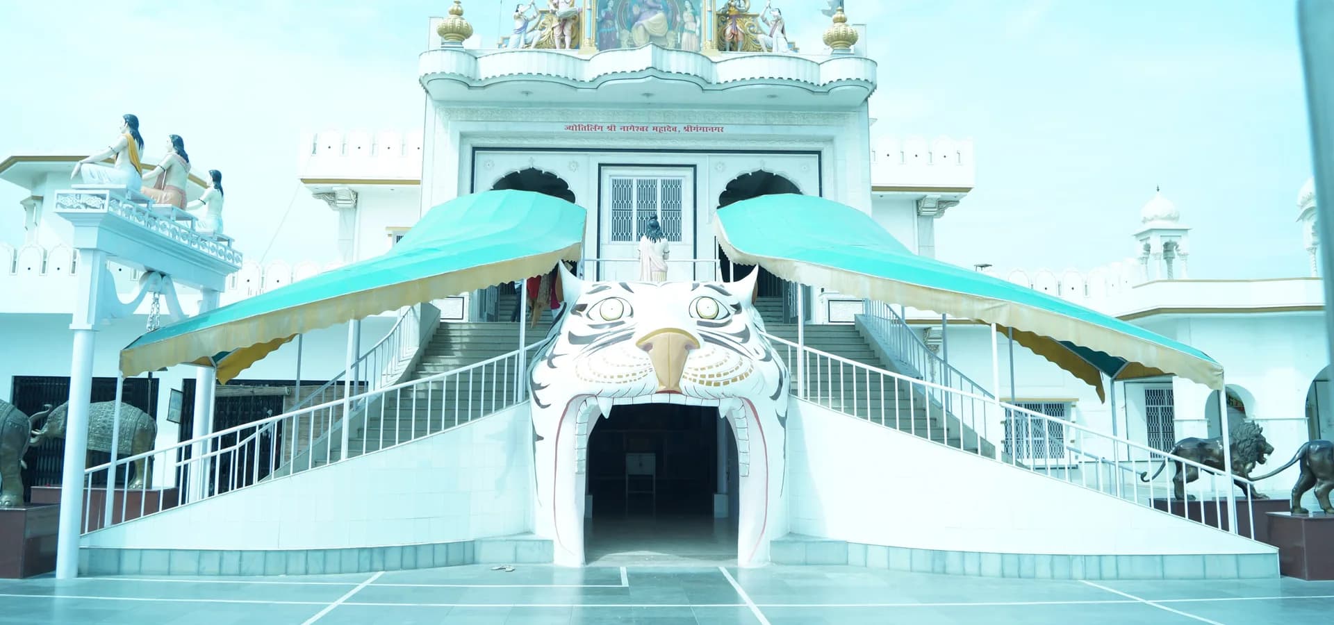 Fachada blanca de un templo en Sri Ganganagar con estatuas en el techo, escaleras gemelas y una entrada con forma de tigre