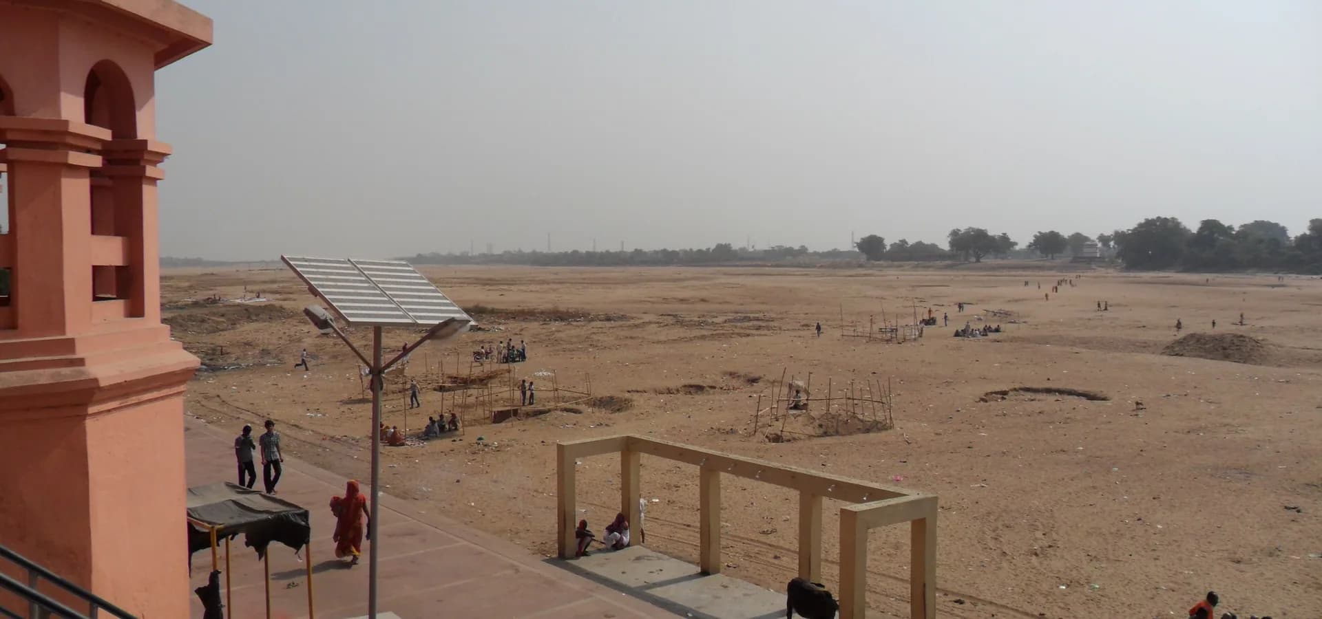 El ancho lecho arenoso del río Phalgu en Gaya, hasta una línea de árboles, con peregrinos en el ghat