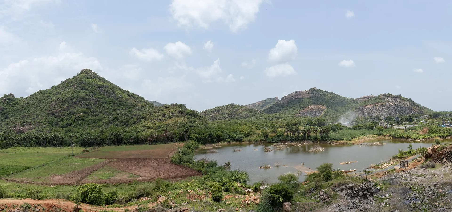 Green hills, farm fields and a quarry lake under a cloudy sky on the outskirts of Guntur