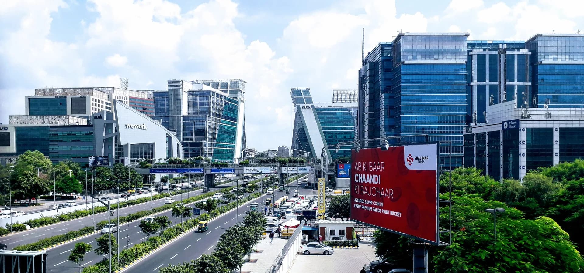 Vista amplia de una autopista arbolada entre las torres de oficinas de cristal de Cyber City en Gurgaon bajo un cielo azul