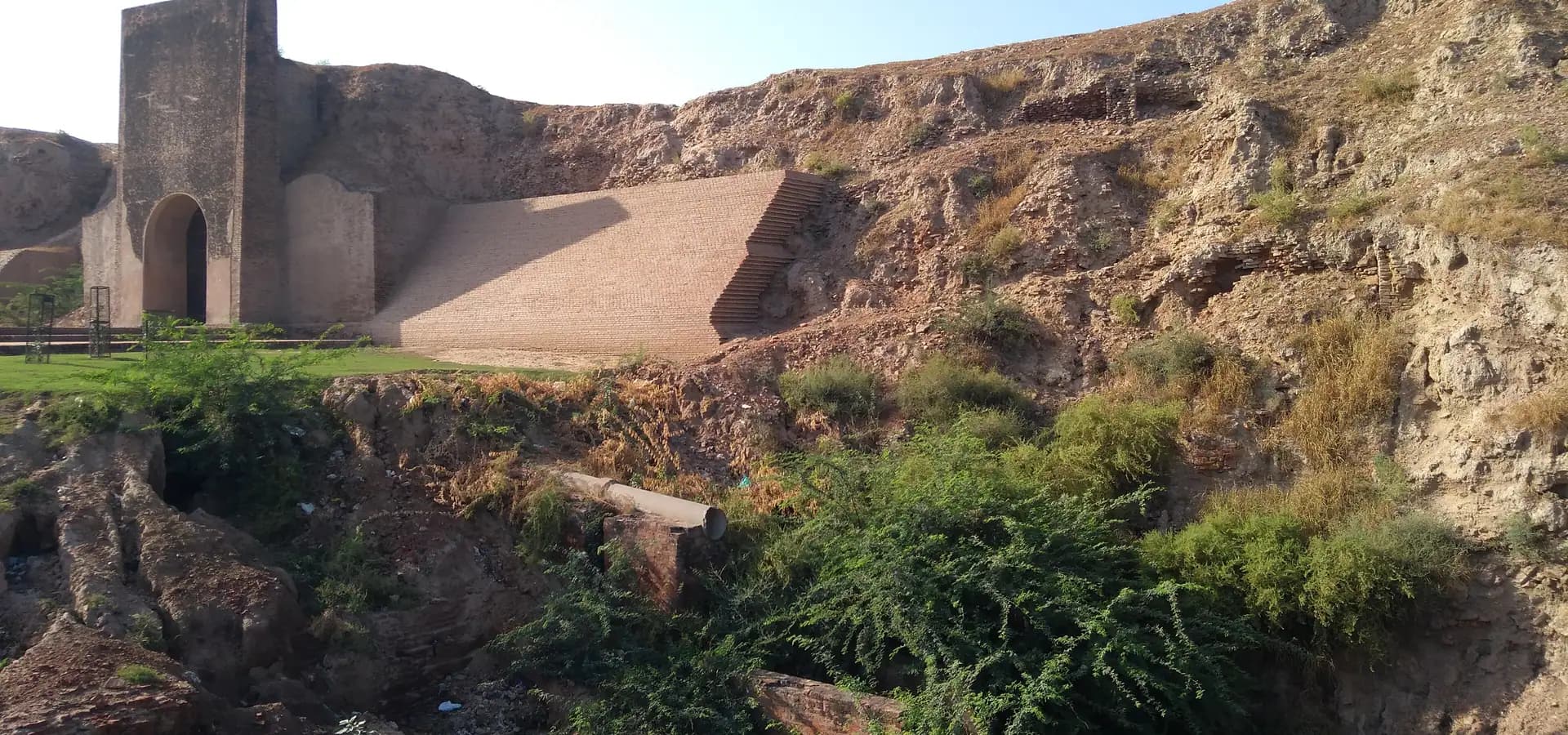 Bröckelnde Erdwälle des Asigarh Fort in Hansi mit Ziegelrampe, altem Torturm und grünen Büschen
