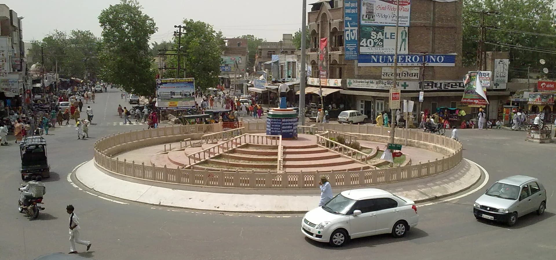 Rotatória Bhagat Singh Chowk em Hanumangarh vista de cima, com lojas, carros e autorriquixás