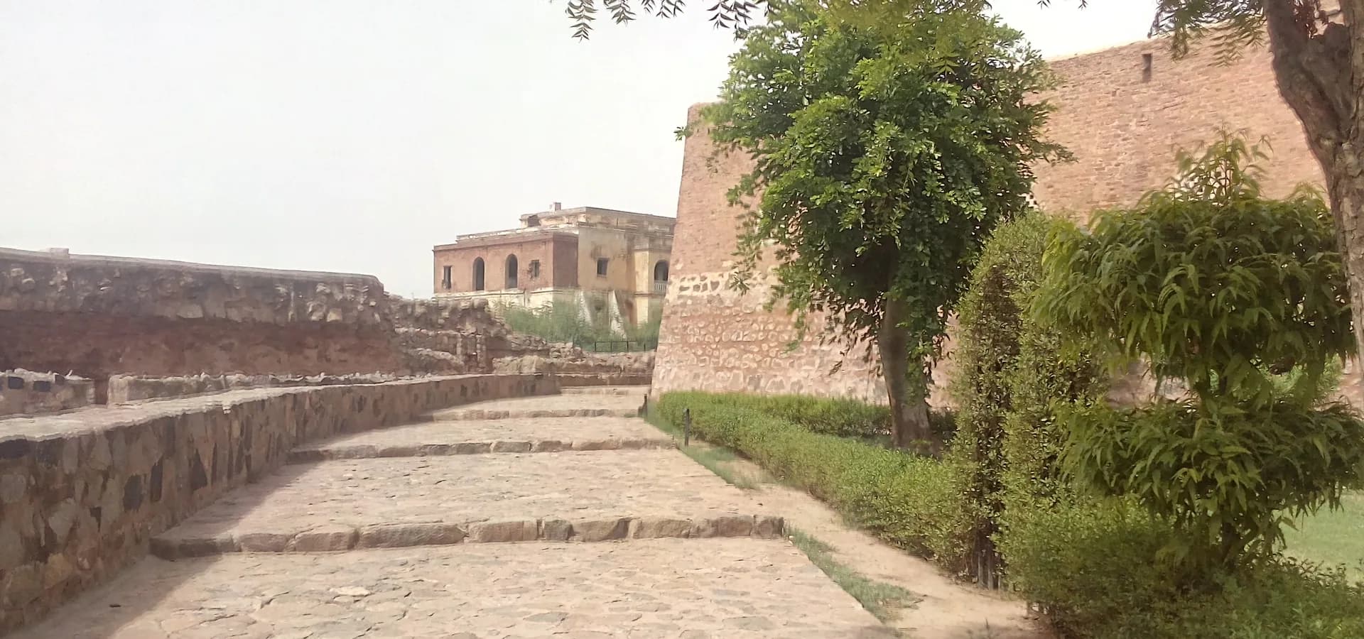 Steinerner Weg entlang der alten Wälle des Palastkomplexes von Firoz Shah in Hisar, mit Bäumen und Festungsmauern