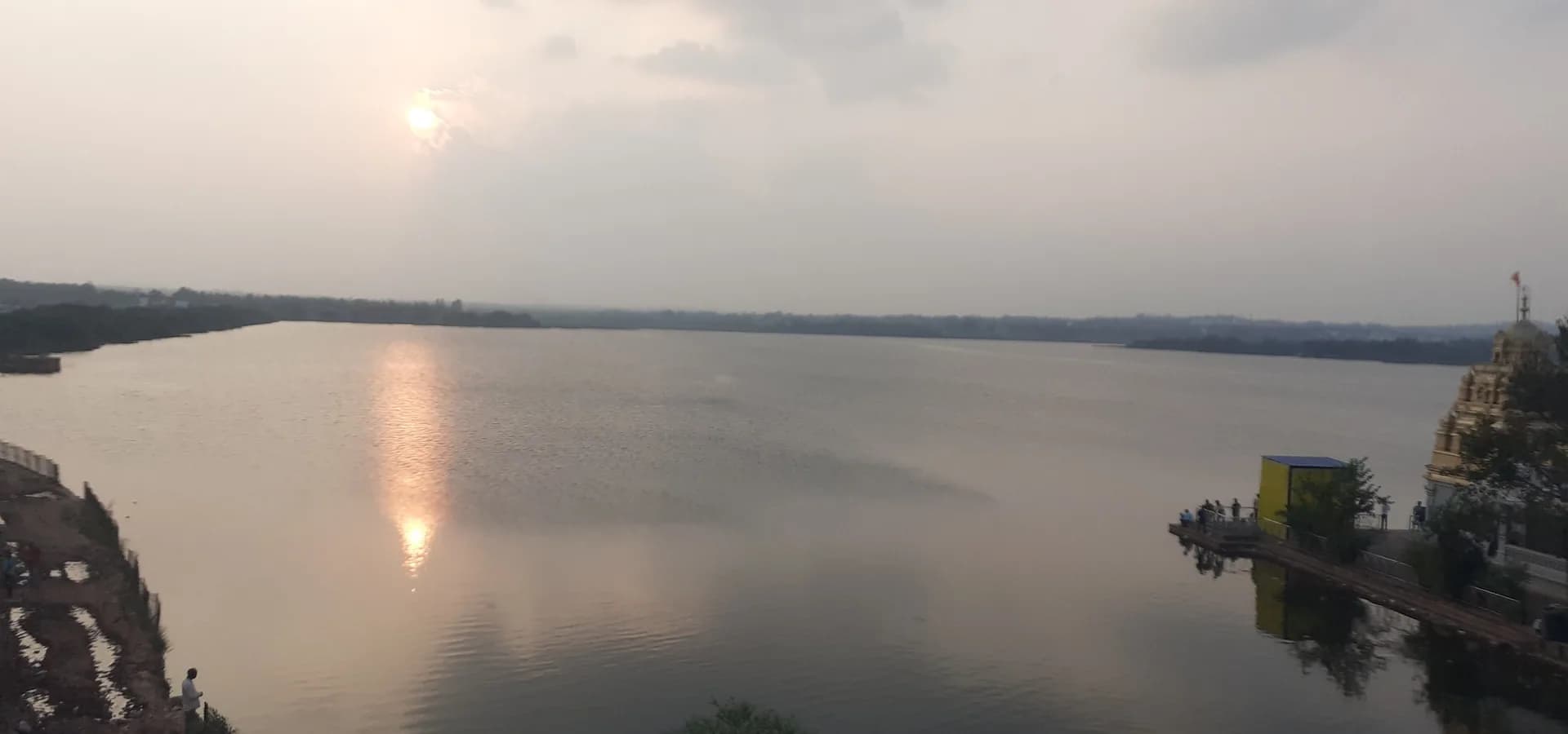 Der Unkal-See in Hubballi bei Sonnenuntergang, die Sonne spiegelt sich im ruhigen Wasser, am rechten Ufer ein Tempelturm