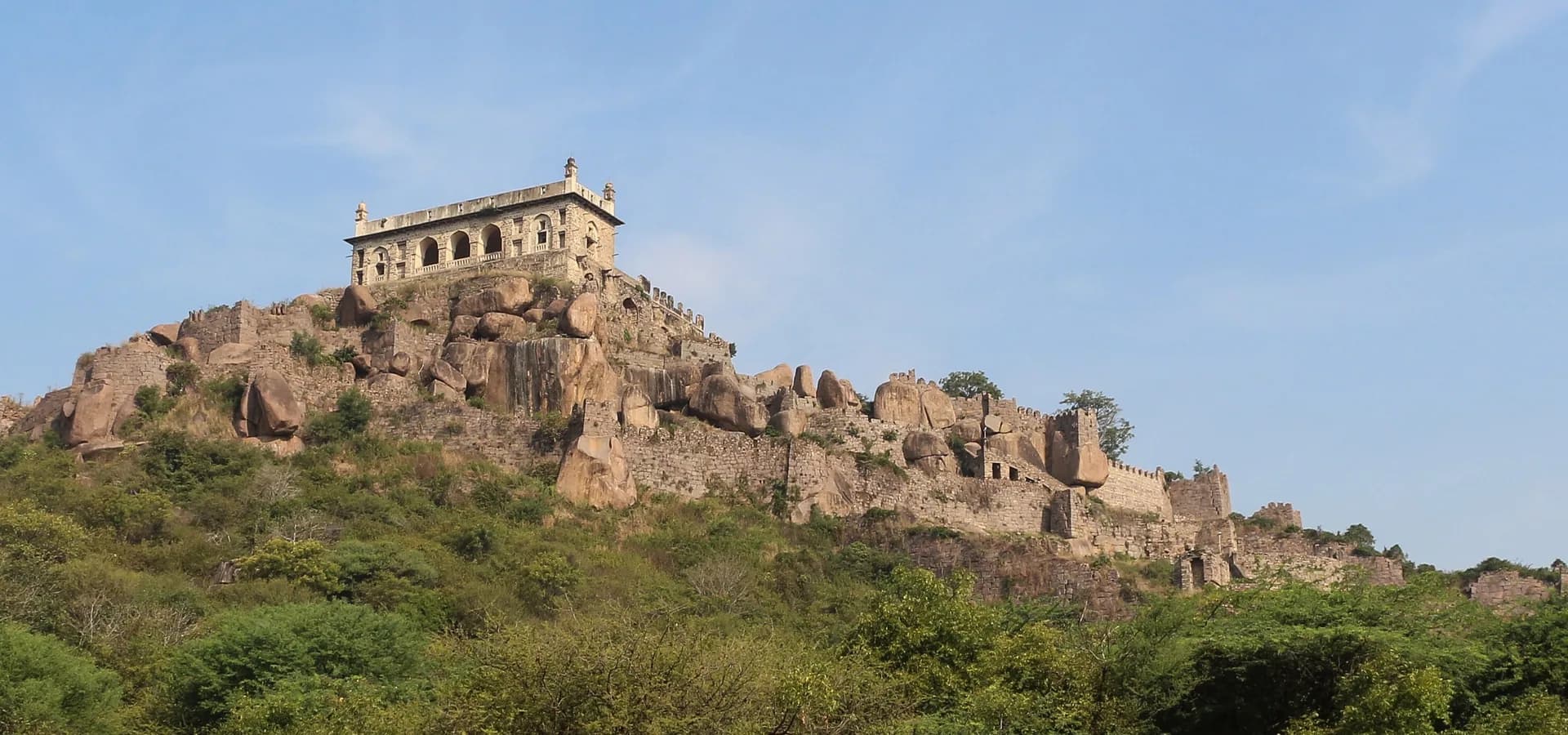 Muralhas do Forte de Golconda e o pavilhão Bala Hisar numa colina de rochedos de granito sobre mato verde