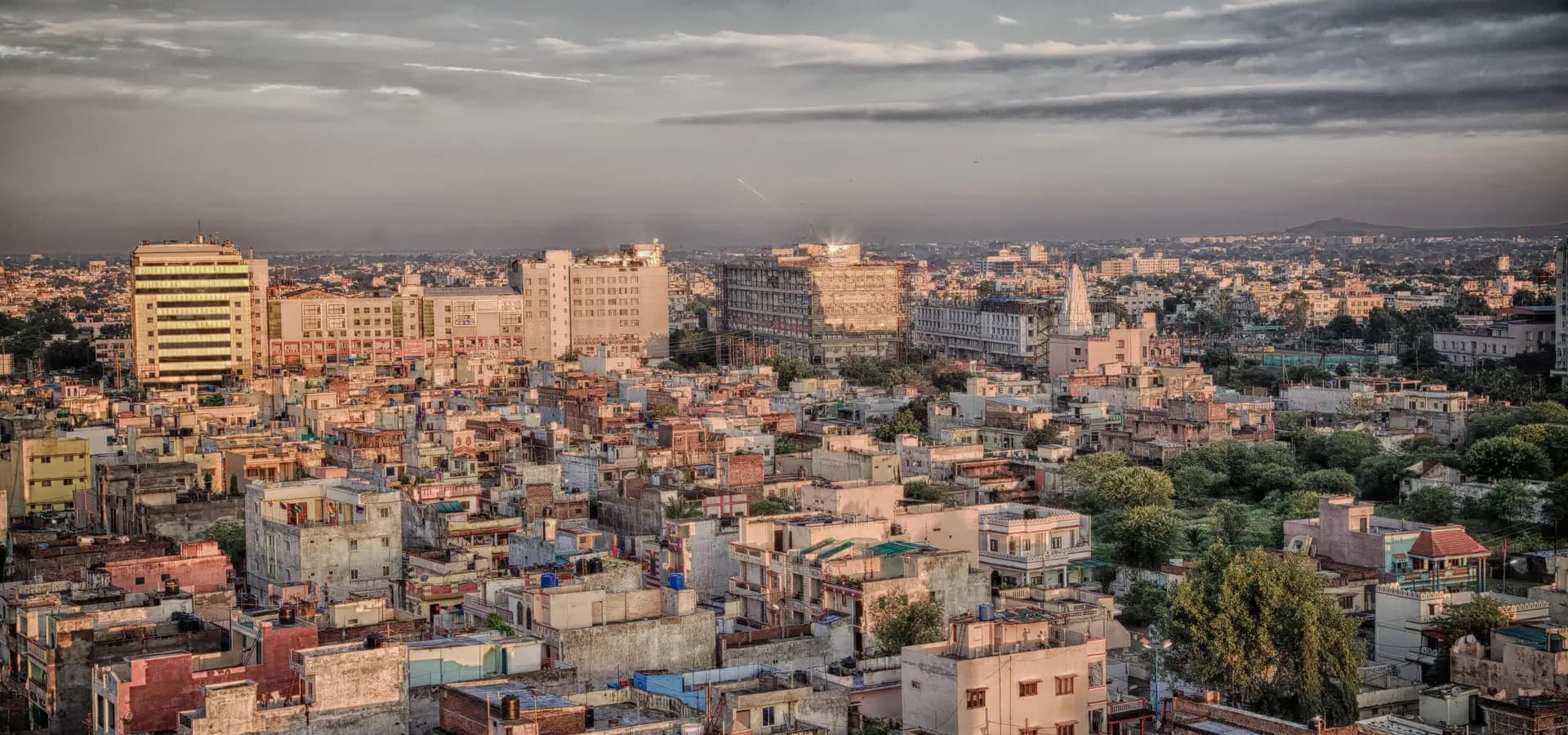 Panorama über Dächer, Bürogebäude und grüne Bäume in Indore unter weitem Himmel im weichen Abendlicht