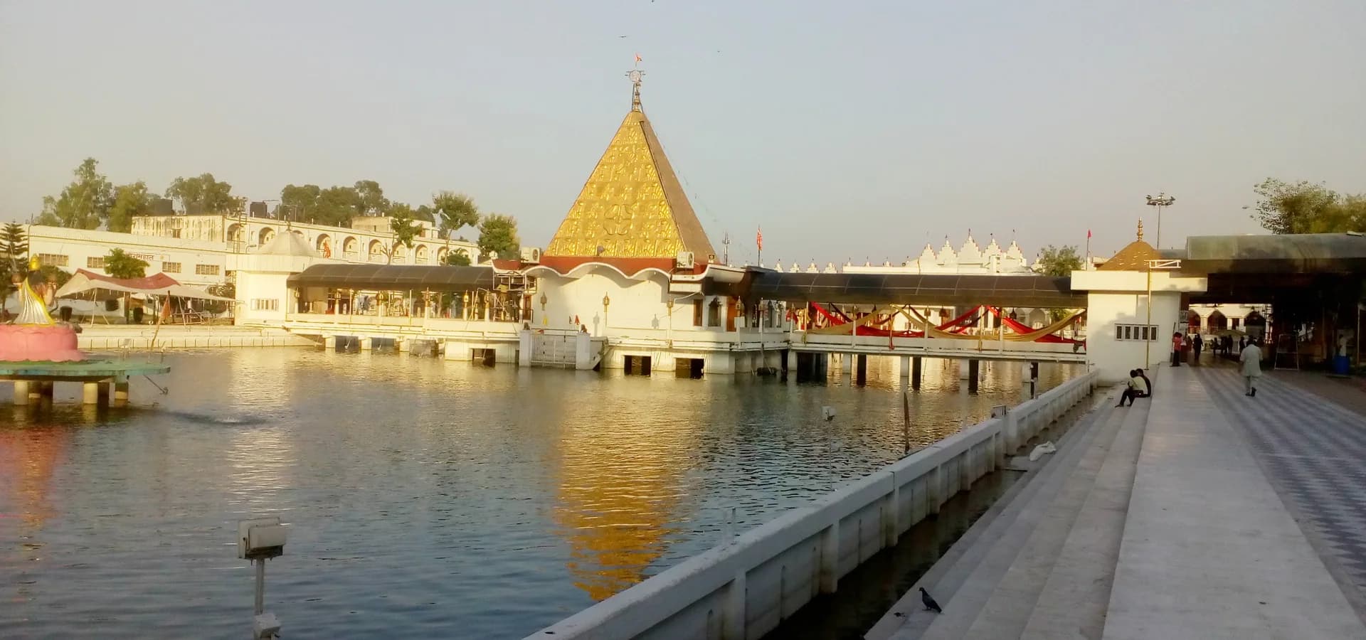 जालंधर में पवित्र तालाब के शांत पानी में झलकती देवी तालाब मंदिर की सुनहरी पिरामिड छत