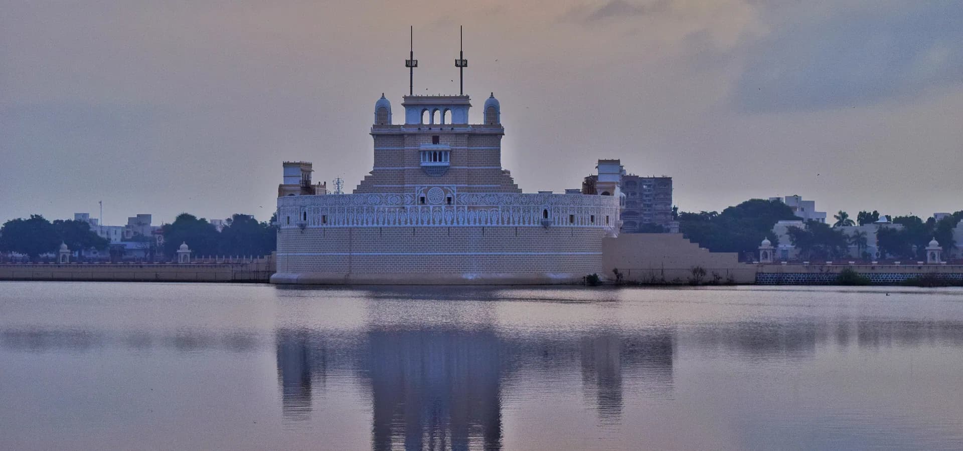 Weißer Lakhota Palace, gespiegelt im ruhigen Wasser des Lakhota Lake unter weichem Abendhimmel in Jamnagar