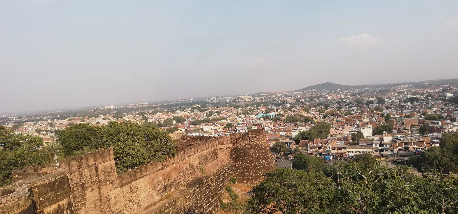 Vista desde el Fuerte de Jhansi sobre sus muros almenados hasta los tejados de la ciudad y una colina baja bajo un cielo pálido