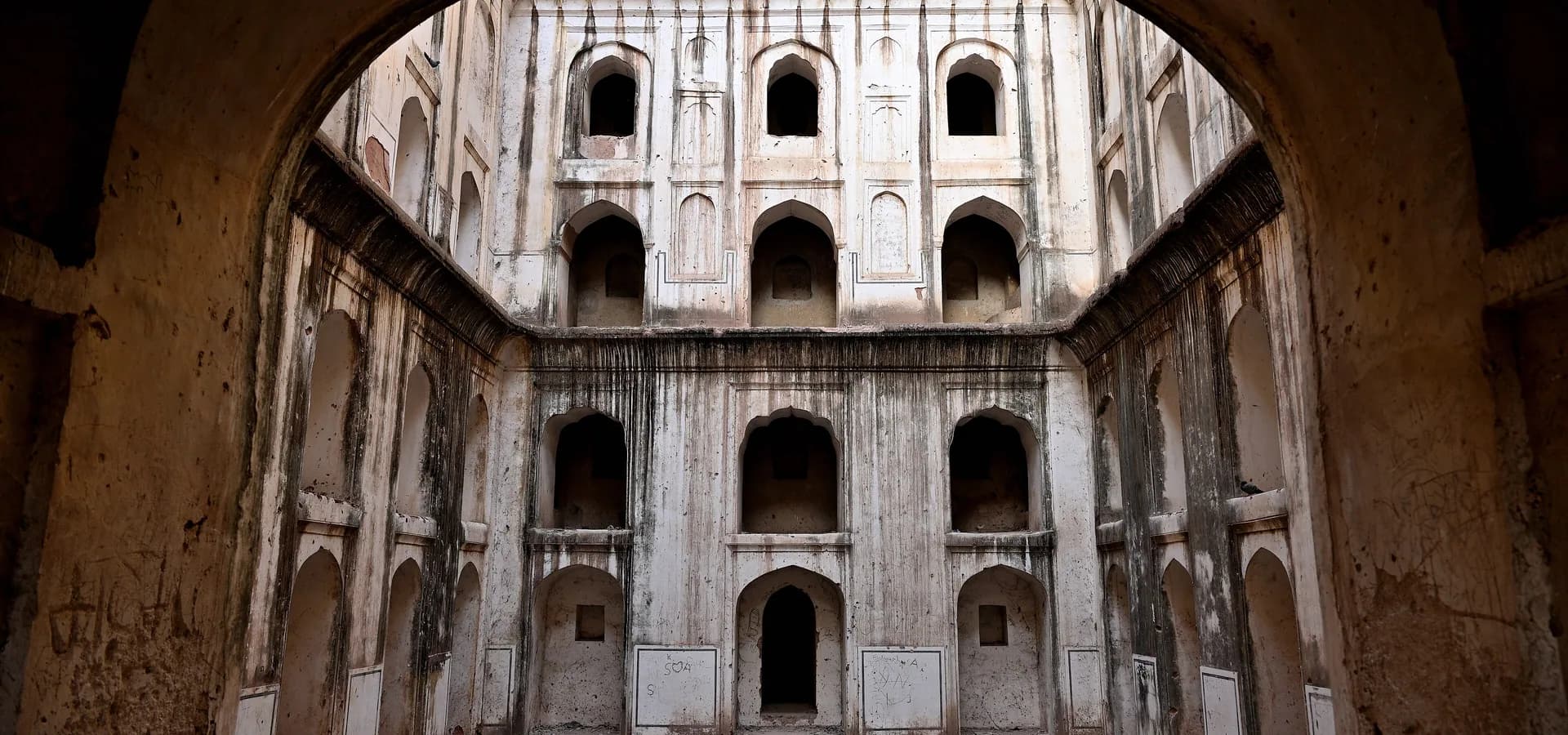 Tiers of arched niches lining the deep shaft of Mertani Baori stepwell, framed by a shadowed stone archway