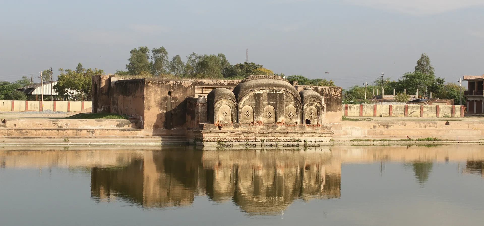 Der Kuppelpavillon des Shukla Talab spiegelt sich in ruhigem Wasser unter blassem Himmel in Akbarpur