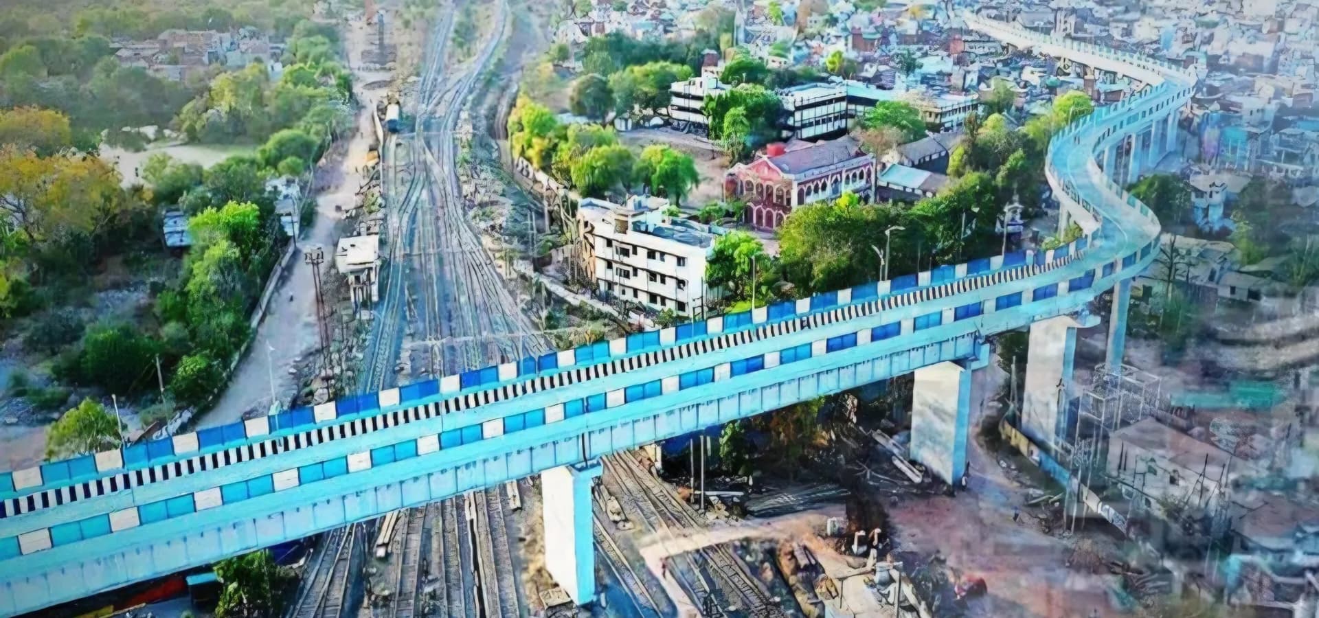 Vista aérea de Katni, com um viaduto ferroviário azul elevado curvando-se sobre os trilhos em direção a telhados e árvores