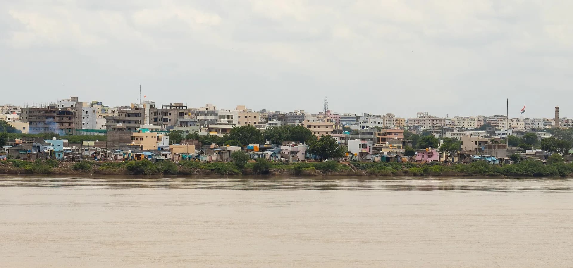 Low-rise buildings of Kurnool lining the far bank of the wide Tungabhadra River under a pale cloudy sky
