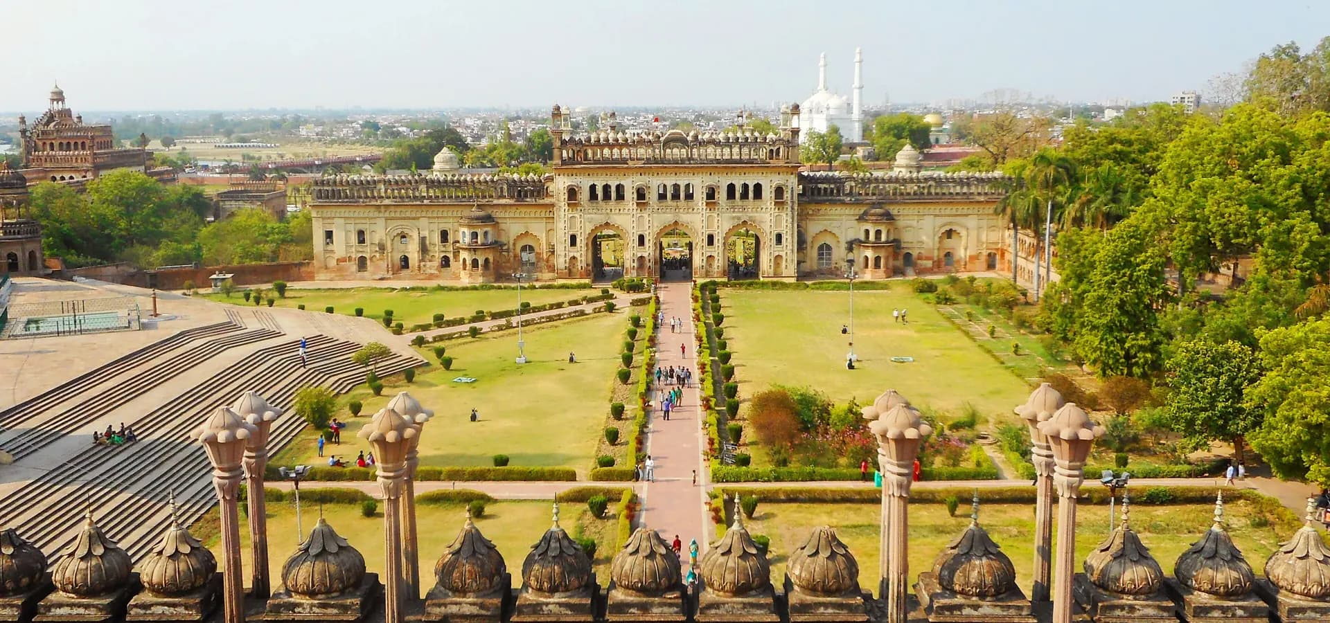 Vista do Bara Imambara sobre gramados verdes, um portão em arco e os telhados planos da velha Lucknow