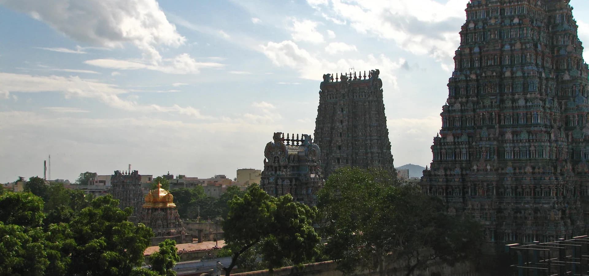 Hohe Gopurams des Meenakshi-Tempels und ein goldenes Schreindach ragen über Bäume unter strahlend blauem Himmel von Madurai