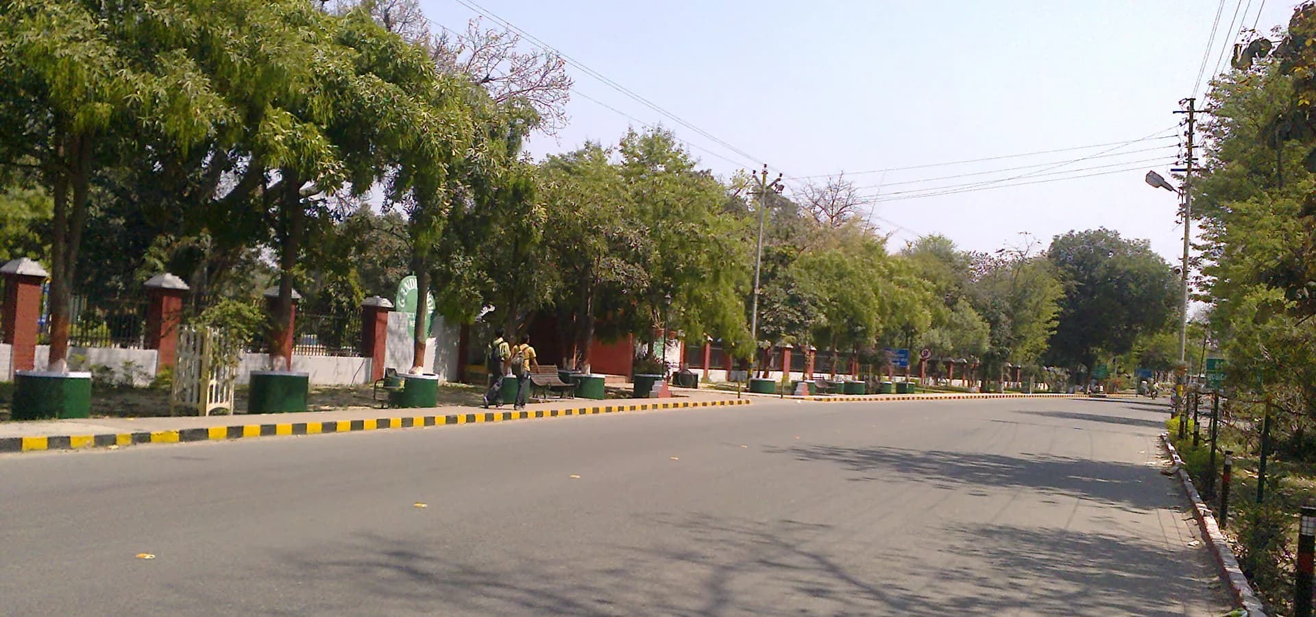 Eine breite, ruhige Mall Road im Cantonment von Meerut, gesäumt von grünen Bäumen unter klarem blauem Himmel