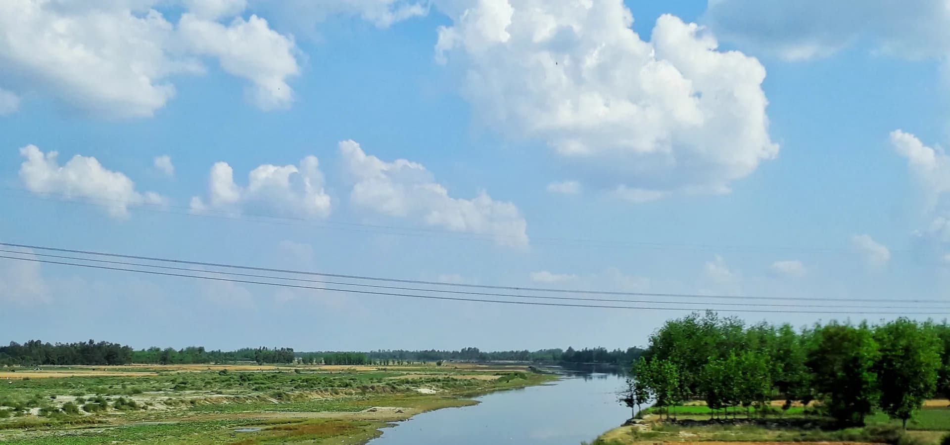Der Fluss Ramganga schlängelt sich unter blauem Himmel mit Quellwolken durch grüne Felder bei Moradabad