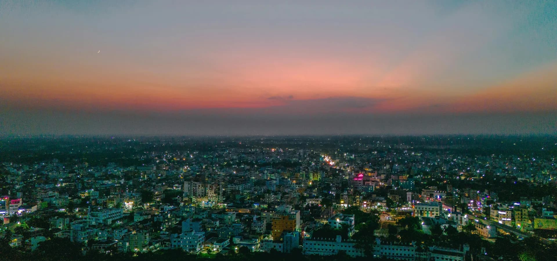 Vista aérea de Muzaffarpur al atardecer, con techos bajos y luces de la ciudad hasta el horizonte bajo un cielo rosado