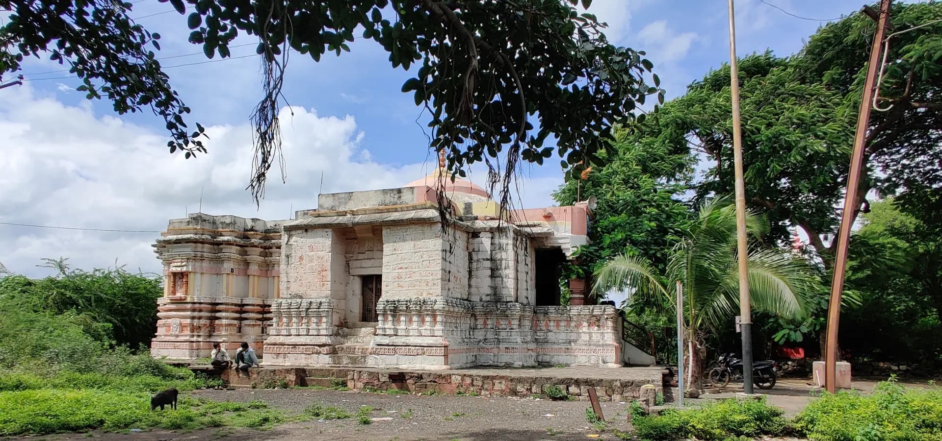 Antigo templo de pedra Kholeshwar entre árvores verdes sob um céu azul nublado em Ambajogai, distrito de Beed