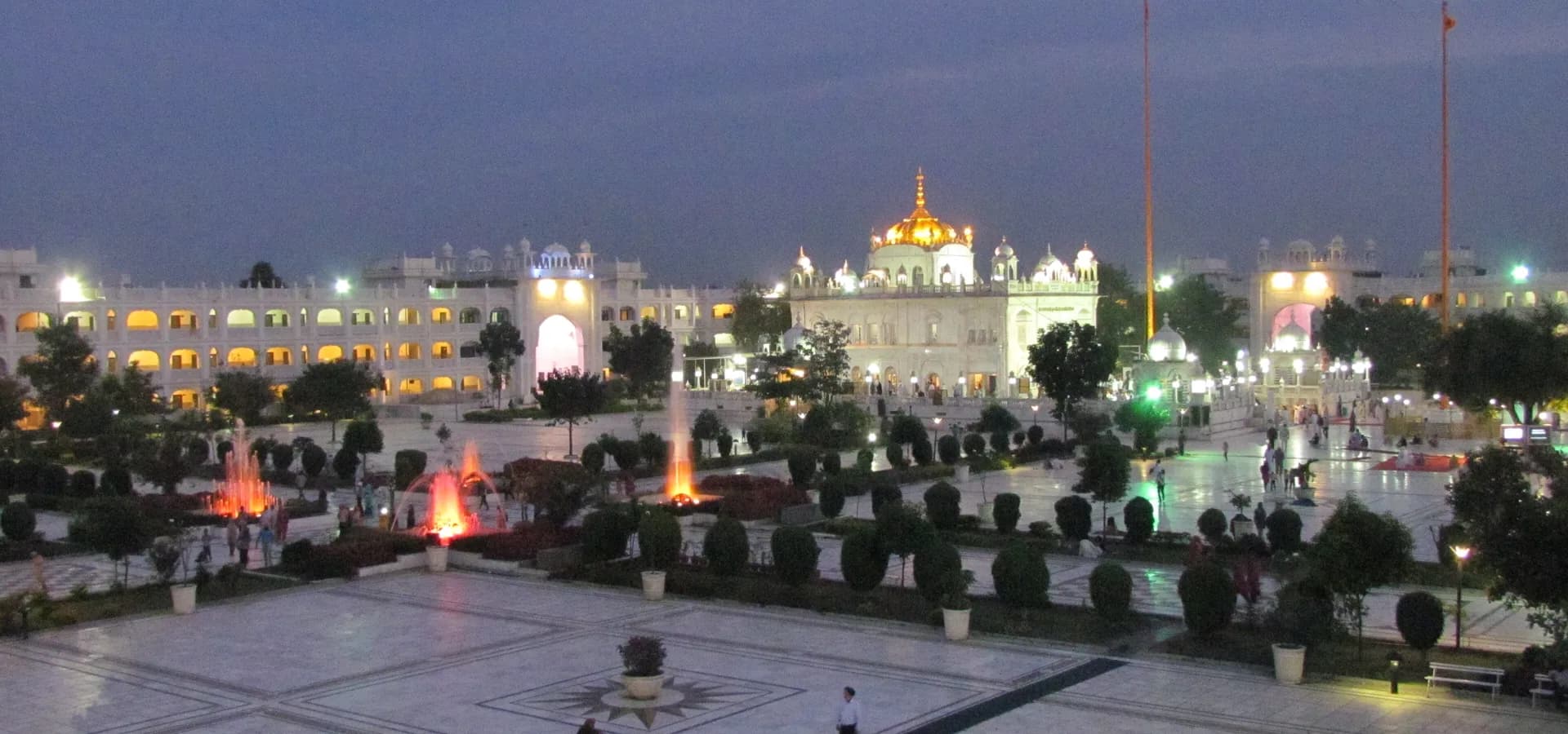 Der Komplex Hazur Sahib in Nanded in der Dämmerung, ein weiter Marmorhof und beleuchtete Brunnen vor dem leuchtenden Heiligtum mit goldener Kuppel
