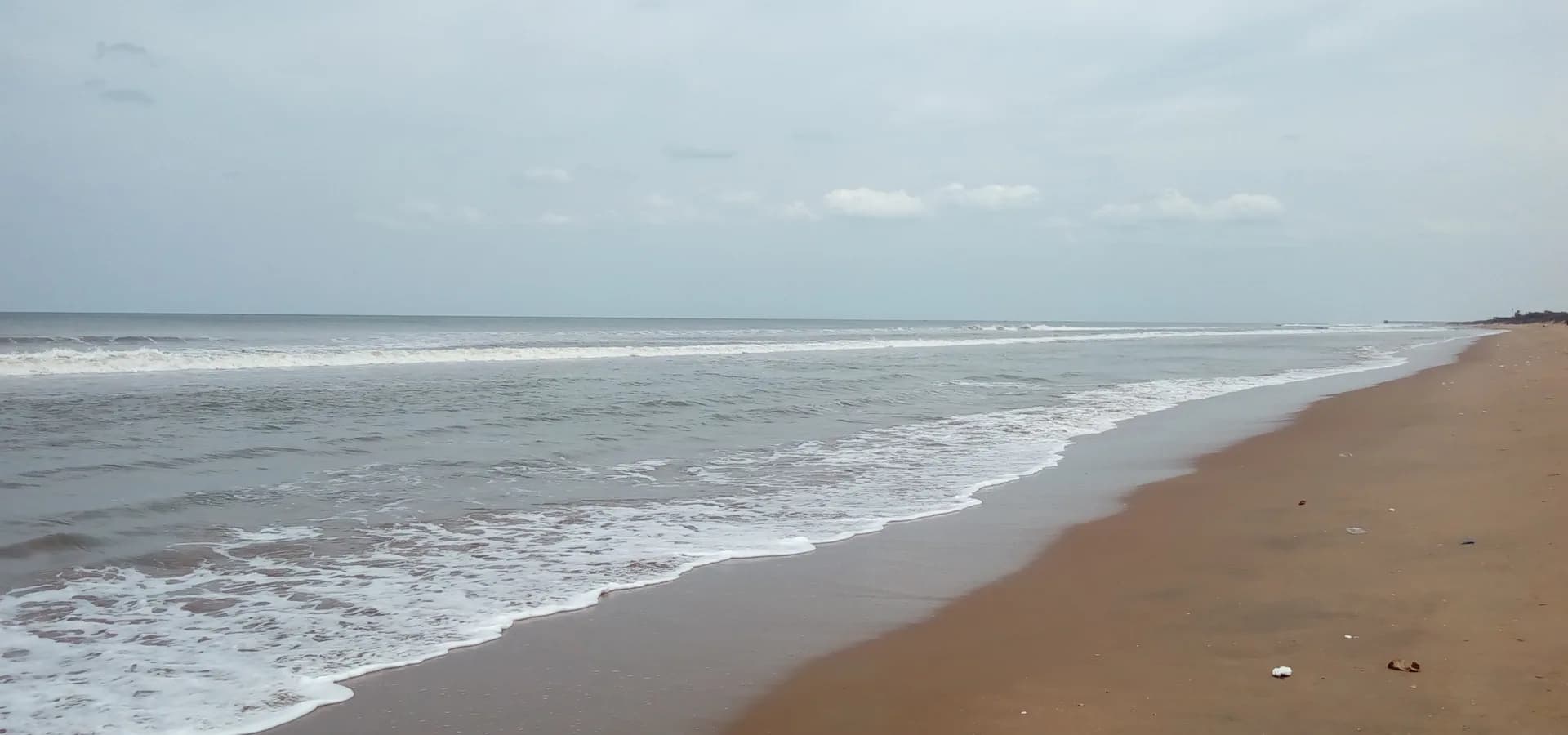 Arena dorada amplia y espuma blanca del golfo de Bengala en la playa de Mypadu, cerca de Nellore, bajo un suave cielo gris
