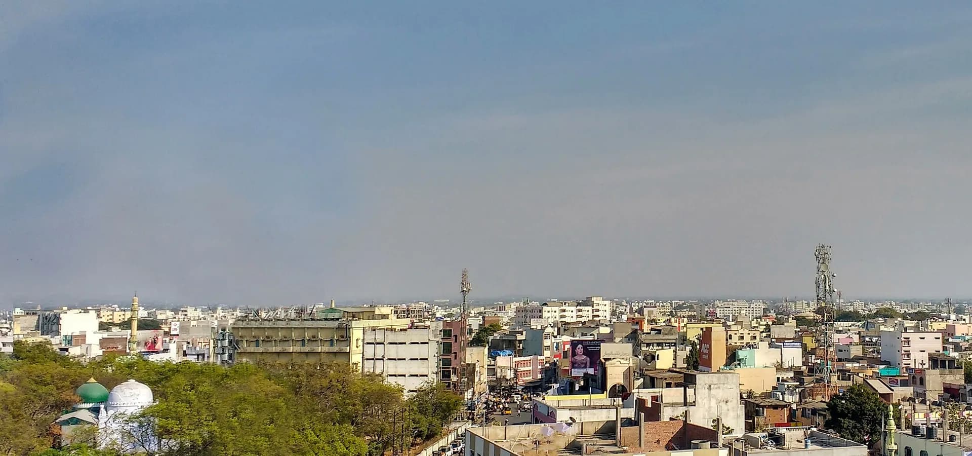 Panorama of Nizamabad, low rooftops and trees stretching to a flat horizon under a wide pale blue sky