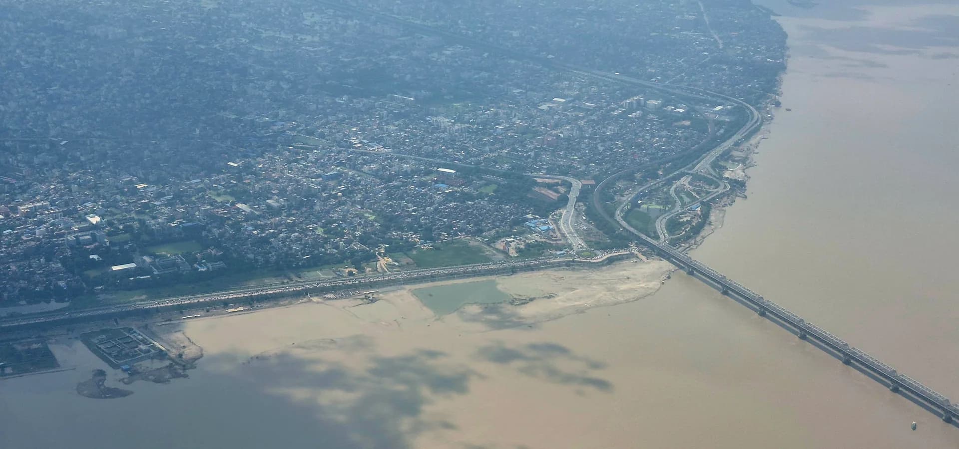 Vista aérea de Patna ao longo do largo Ganges, com vias à beira do rio e uma longa ponte atravessando a água