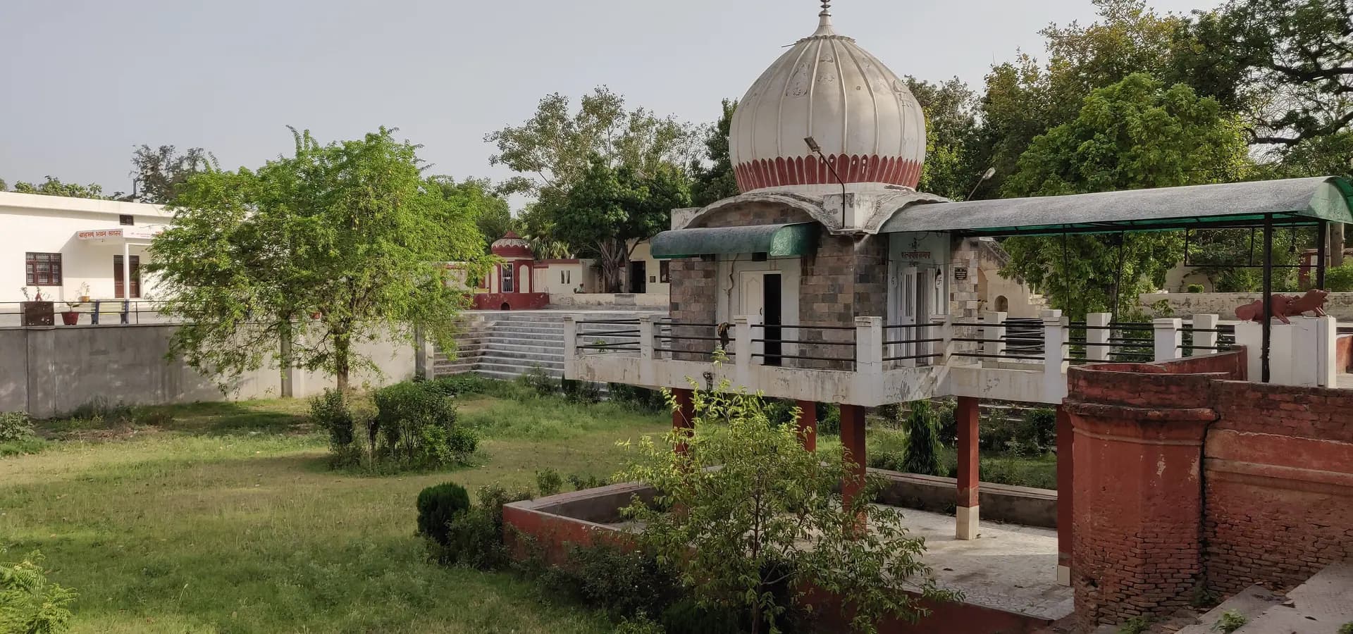 Weiße gerippte Kuppel des Rajrajeshwari-Tempels in Sangrur über Rasen, Sträuchern und roten Backsteinstufen