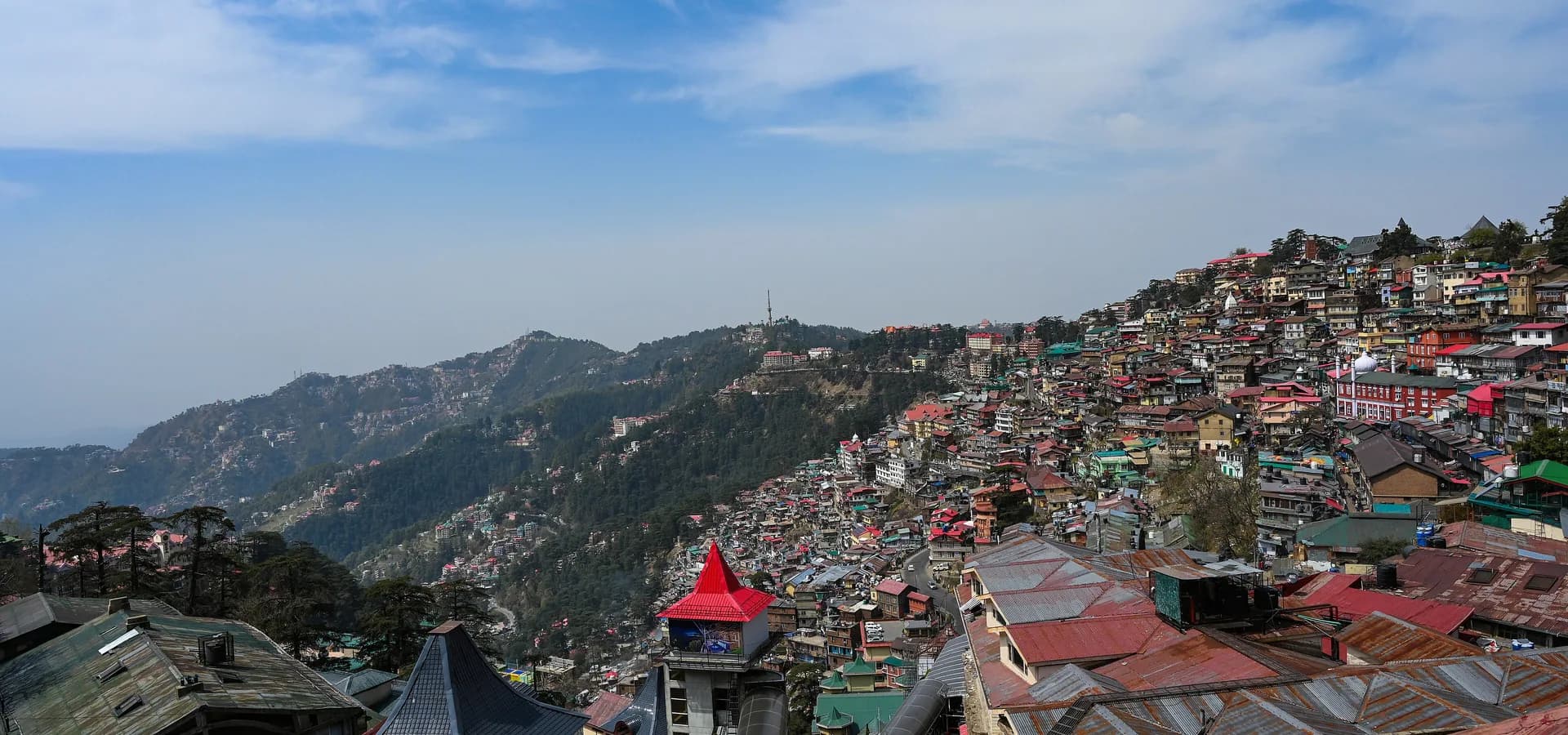 Telhados coloridos de Shimla subindo uma encosta íngreme ao lado de cristas florestadas do Himalaia sob céu azul
