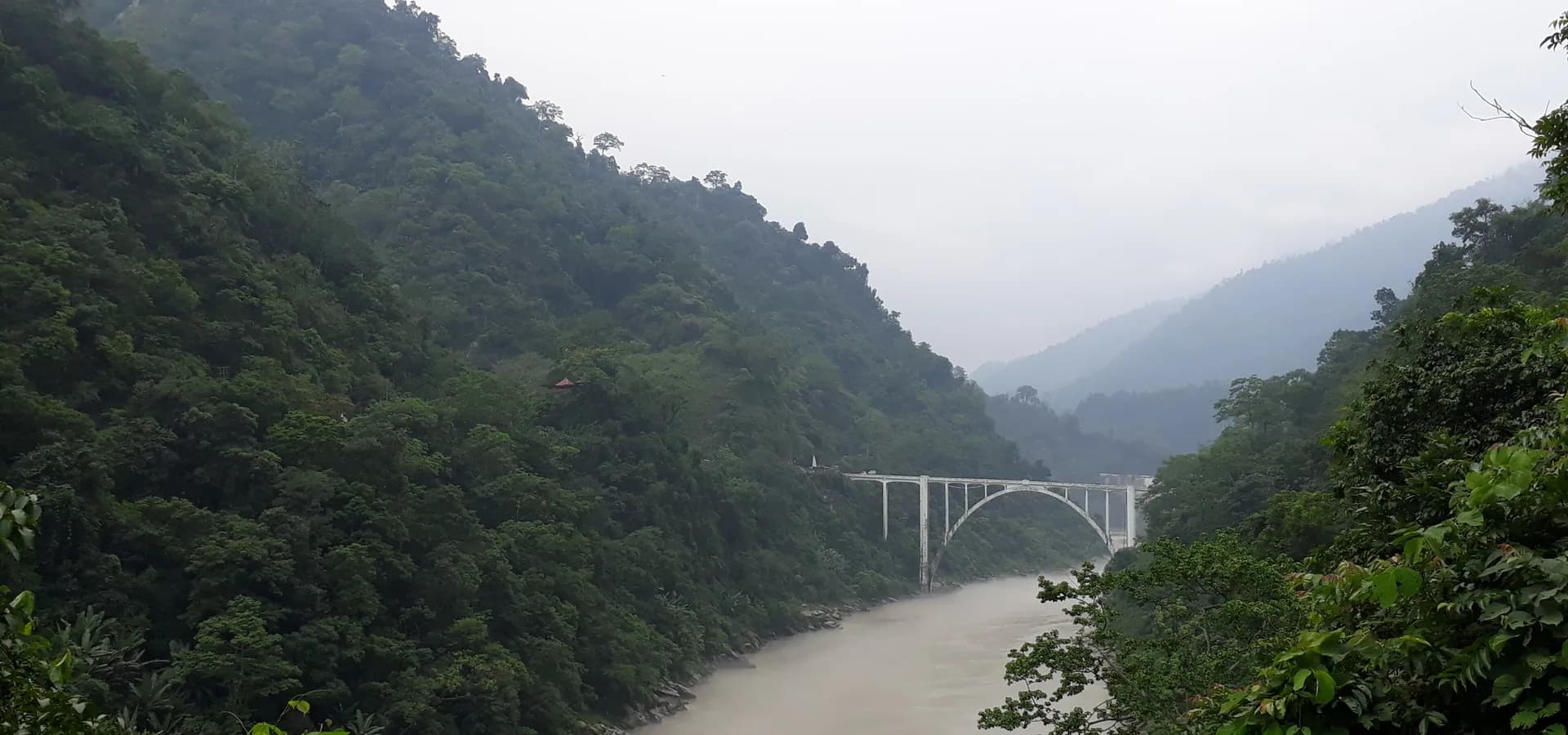Weißer Betonbogen der Coronation Bridge über der Teesta in einer grünen, nebligen, bewaldeten Schlucht