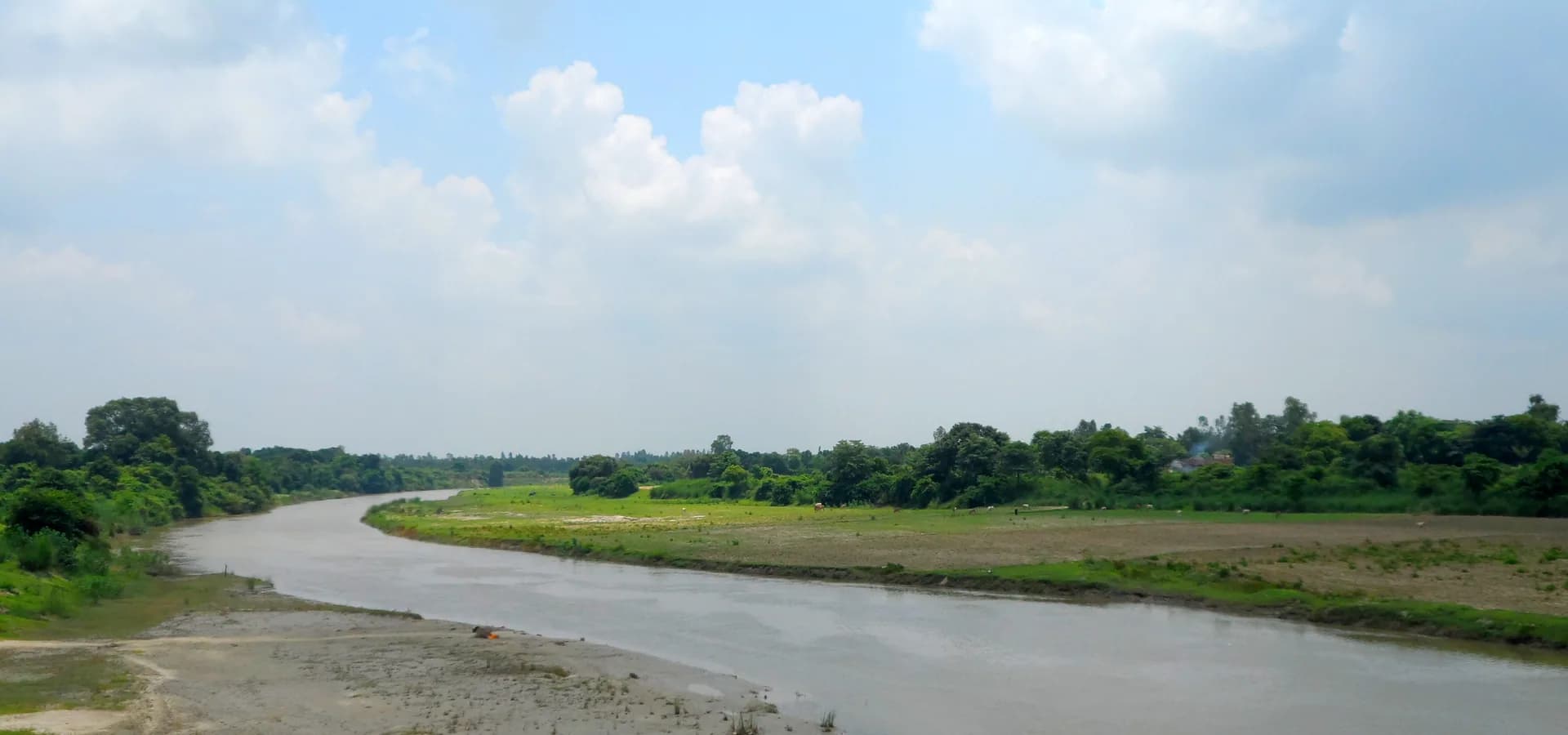 El río Gomti serpenteando entre campos verdes y árboles cerca de Sitapur bajo un cielo azul nublado