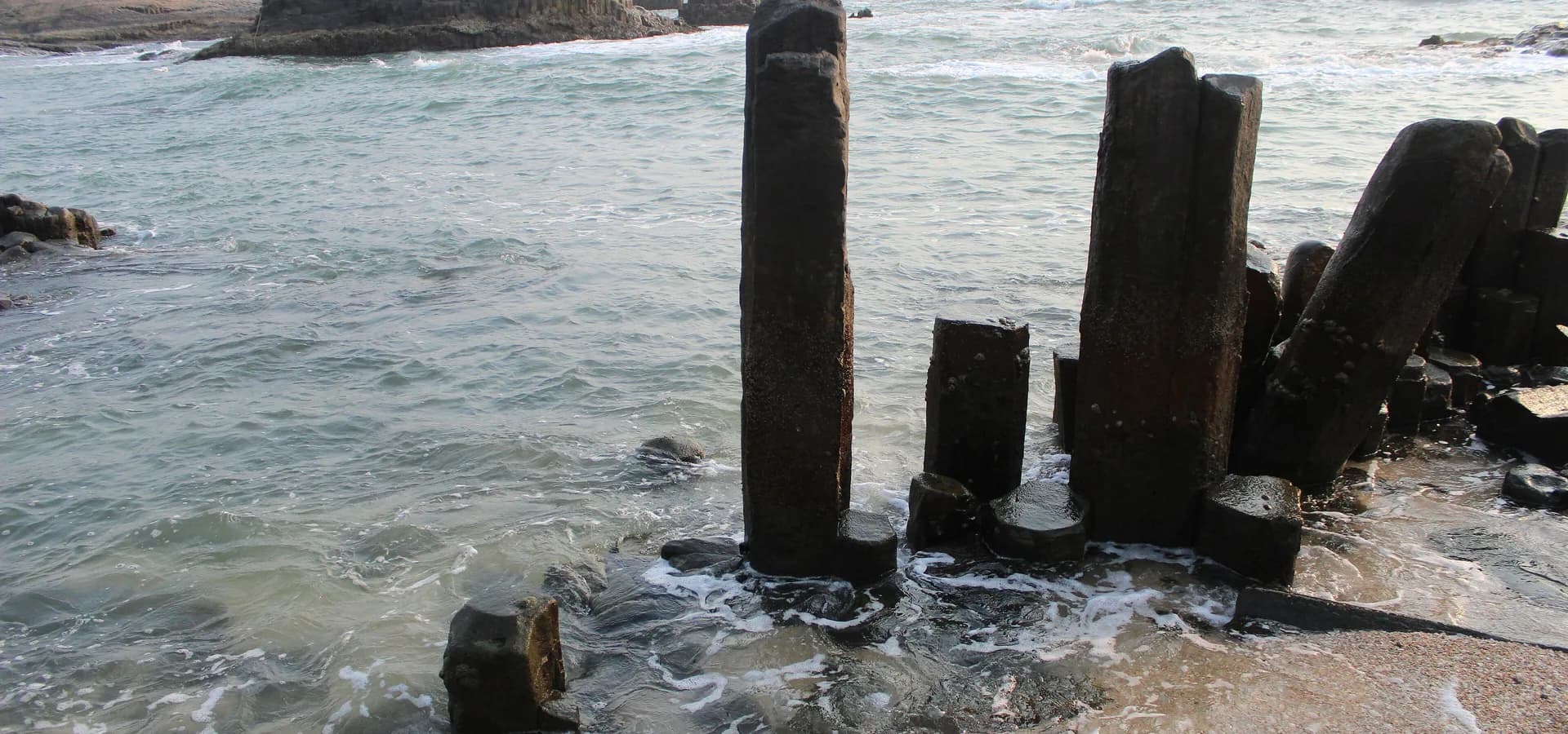 Altas columnas de basalto oscuro que emergen de las olas en la isla de St Mary, cerca de Udupi, con el mar en calma al fondo