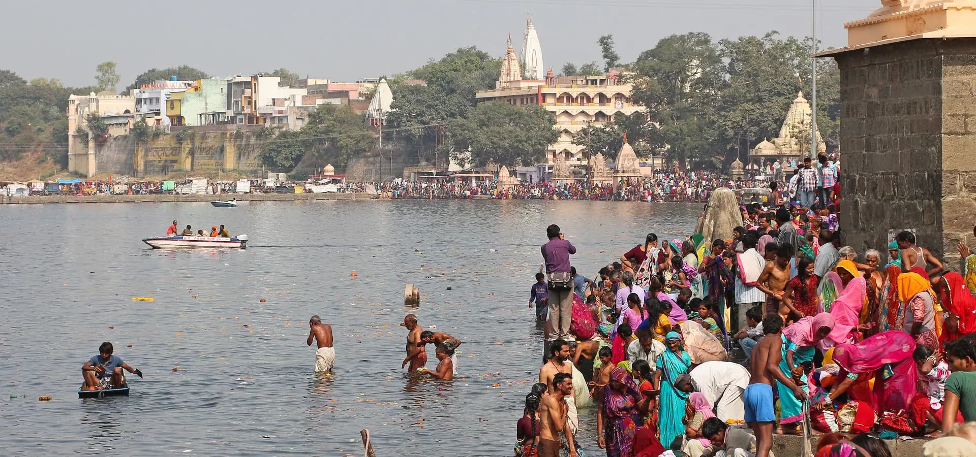 Pilgrims bathing on the steps of Ram Ghat as the Shipra River stretches toward temple spires on the far bank