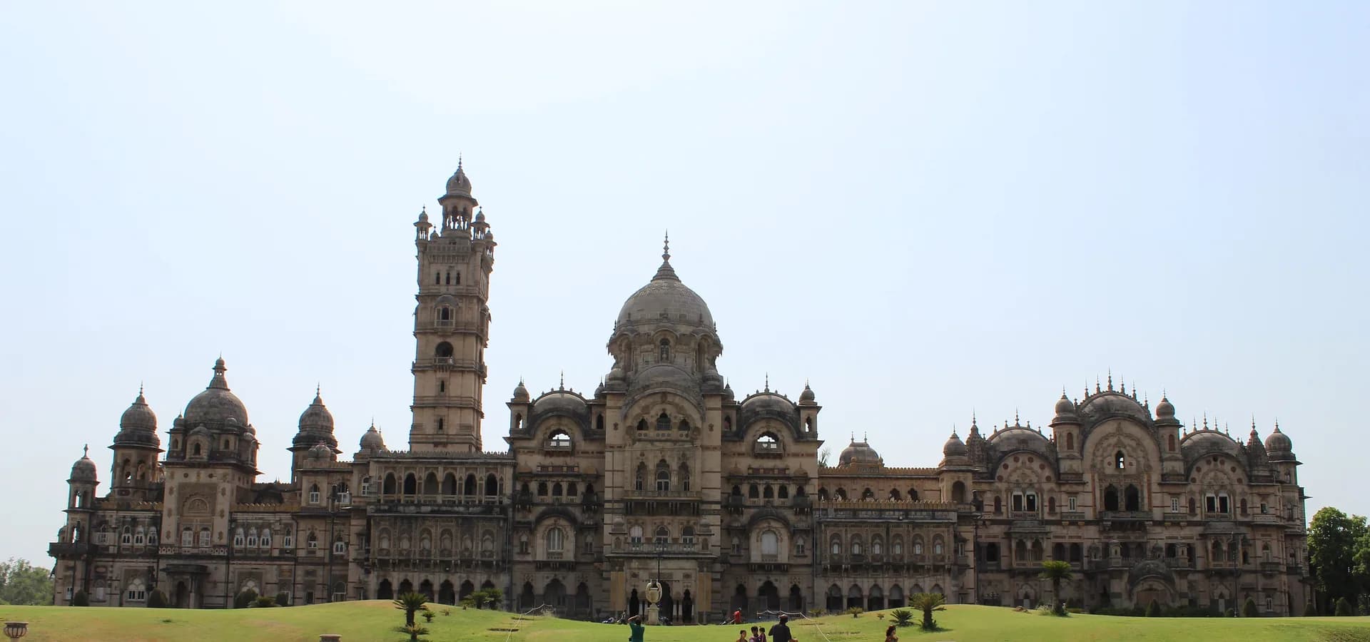 Laxmi-Vilas-Palast in Vadodara, eine lange indo-sarazenische Fassade mit Kuppeln und hohem Turm über grünen Rasenflächen
