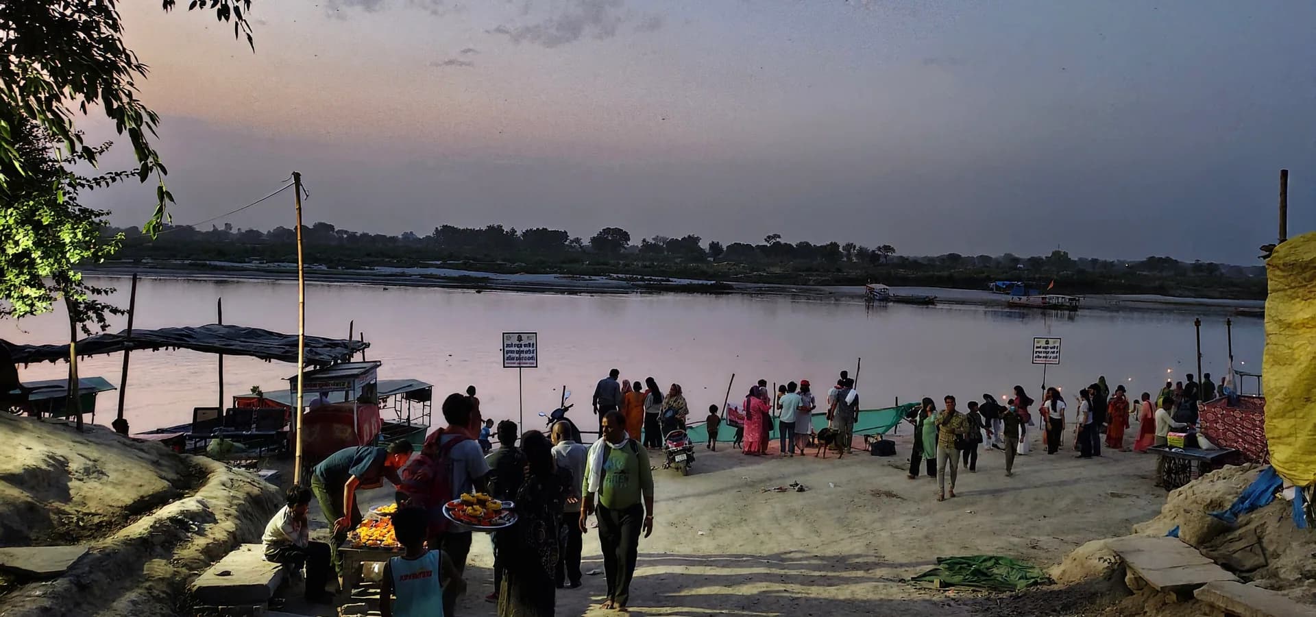 Die breite Yamuna in der Dämmerung vom Kesi Ghat in Vrindavan, mit festgemachten Booten und Pilgern am Ufer