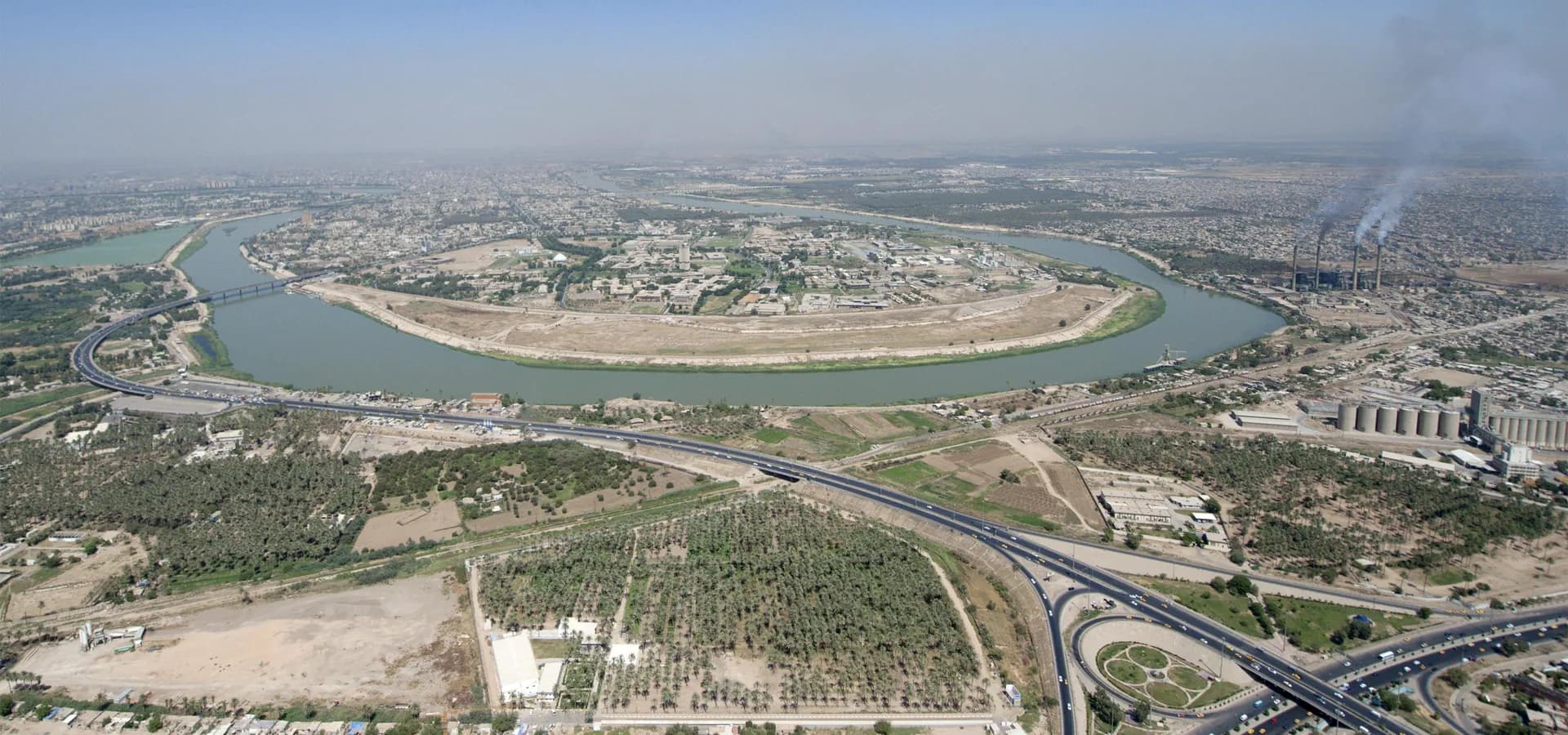 Vista aérea del Tigris serpenteando por Bagdad entre palmerales, calles y manzanas bajas de la ciudad