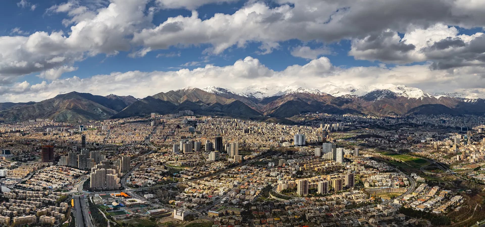 Weites Luftpanorama des nördlichen Teheran, Häuserreihen und Türme unter schneebedeckten Alborz-Gipfeln und großen Wolken