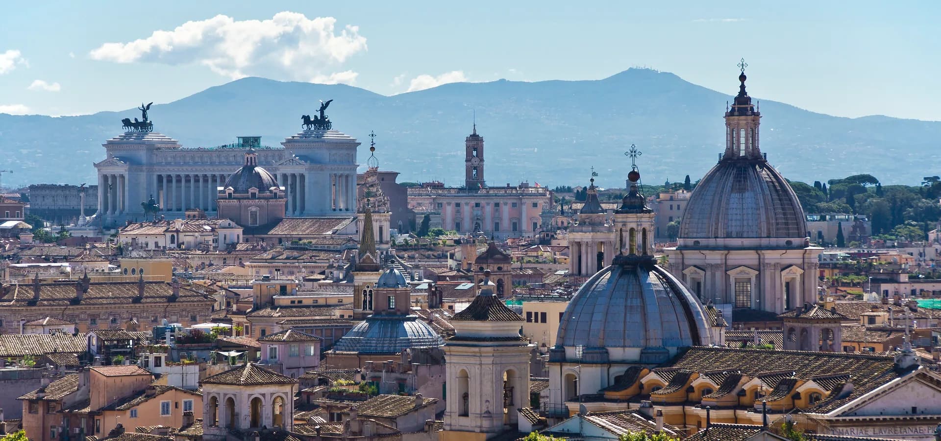 Kuppeln und Terrakottadächer des Zentrums von Rom, das weiße Vittoriano und blaue Albaner Berge unter klarem Himmel
