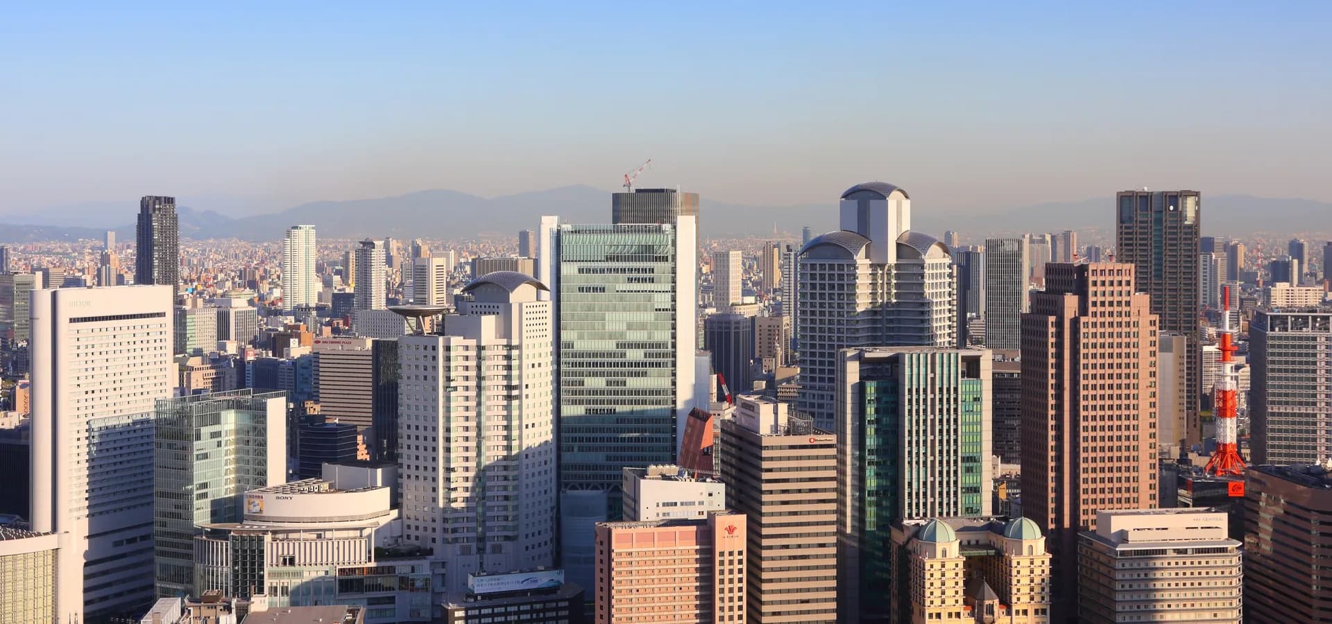 Wolkenkratzer im Stadtteil Umeda unter klarem Himmel, die Stadt breitet sich bis zu fernen Bergen aus