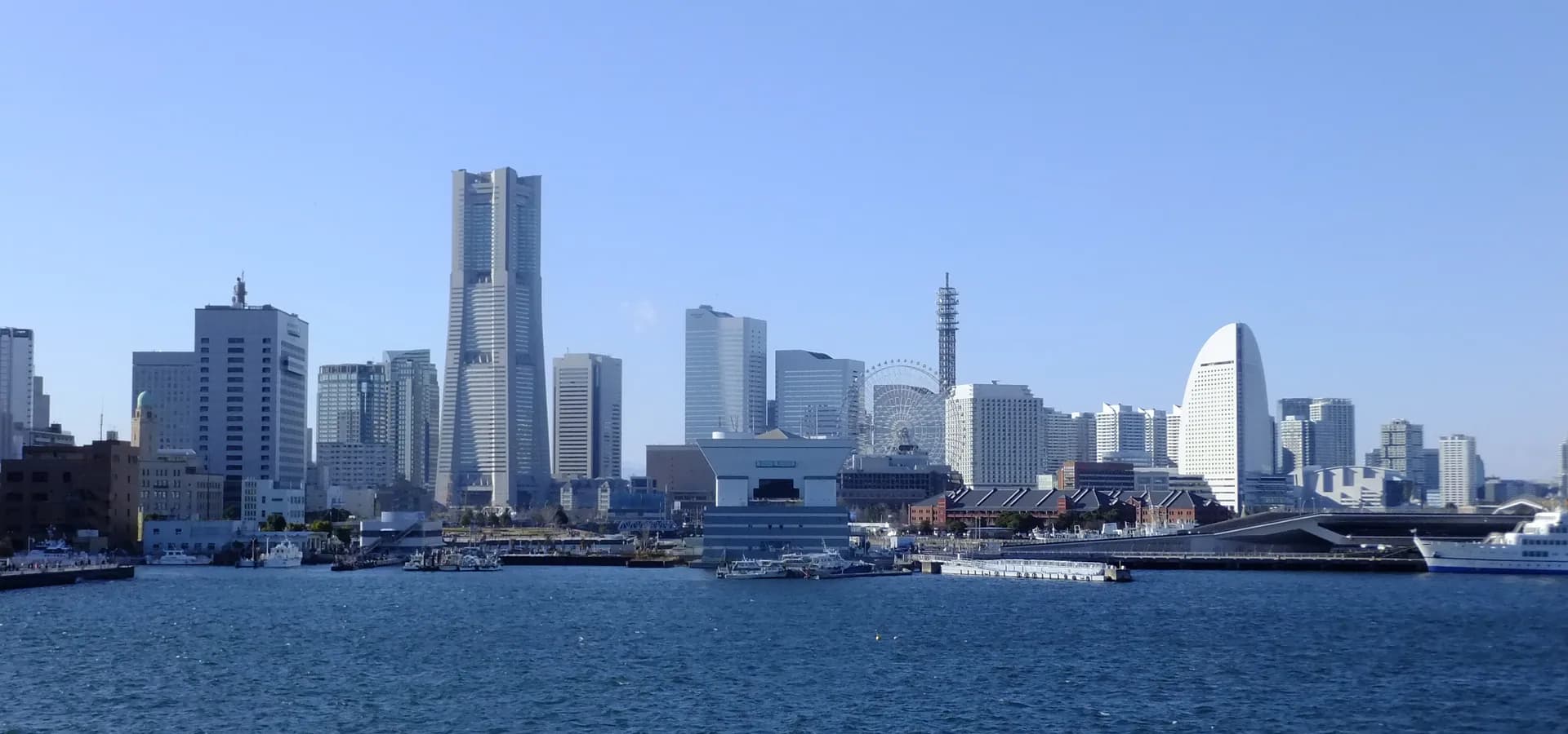 Horizonte de Minato Mirai com a Landmark Tower, uma roda-gigante e um hotel em forma de vela sobre as águas azuis do porto