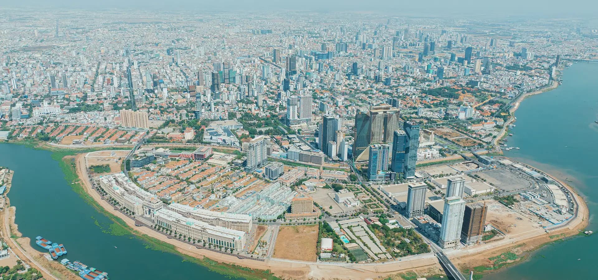 Luftaufnahme von Koh Pich mit der Skyline von Phnom Penh dahinter, umgeben von breiten Flussarmen