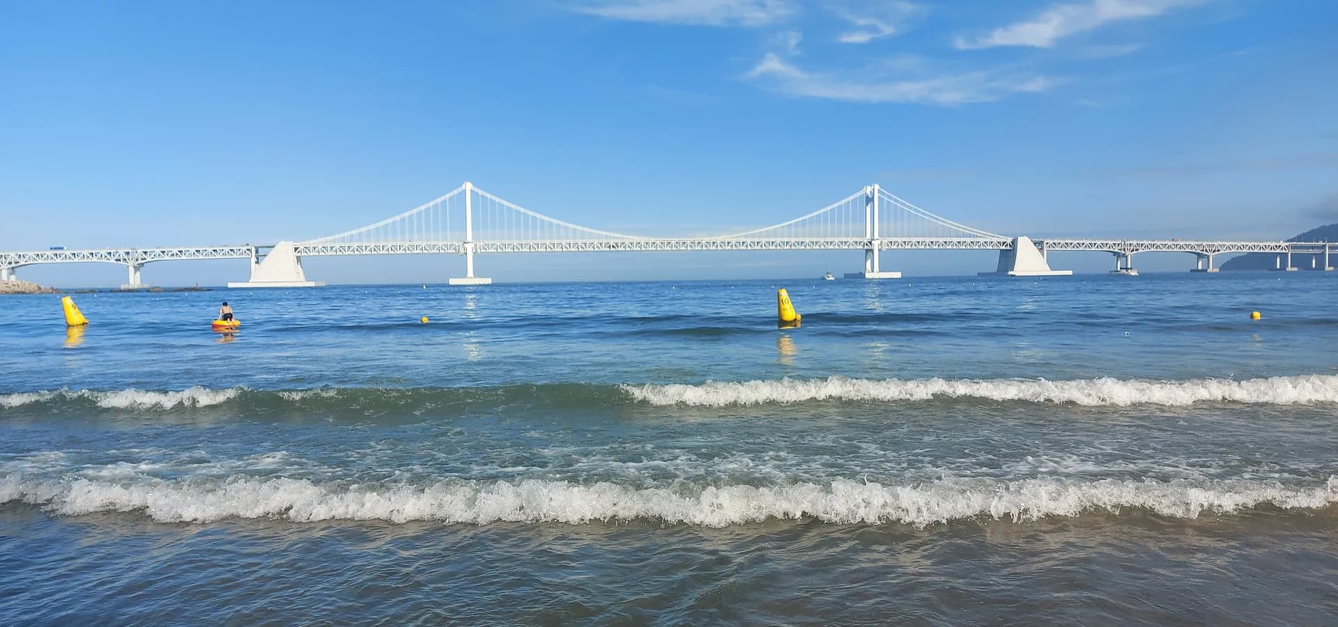 Weiße Gwangan-Hängebrücke über einer blauen Bucht, gesehen aus der Brandung am Gwangalli-Strand in Busan