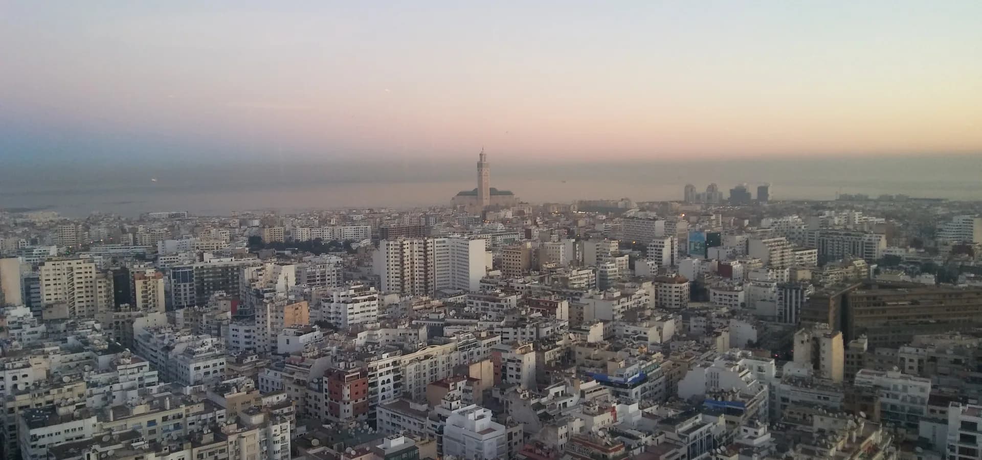 Pale dawn sky over the white rooftops of Casablanca, with the Hassan II Mosque minaret on the Atlantic shore