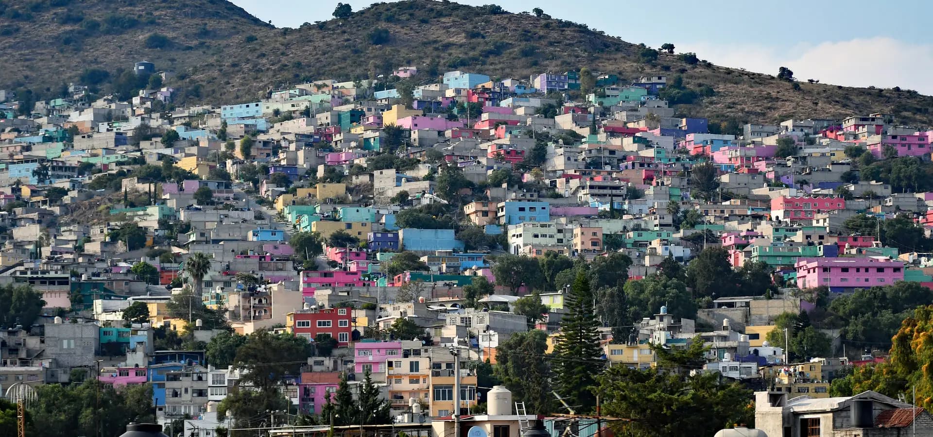 Rosa, blaue und gelbe Häuser, die sich einen trockenen Hang der Sierra de Guadalupe in Ecatepec hinaufstapeln