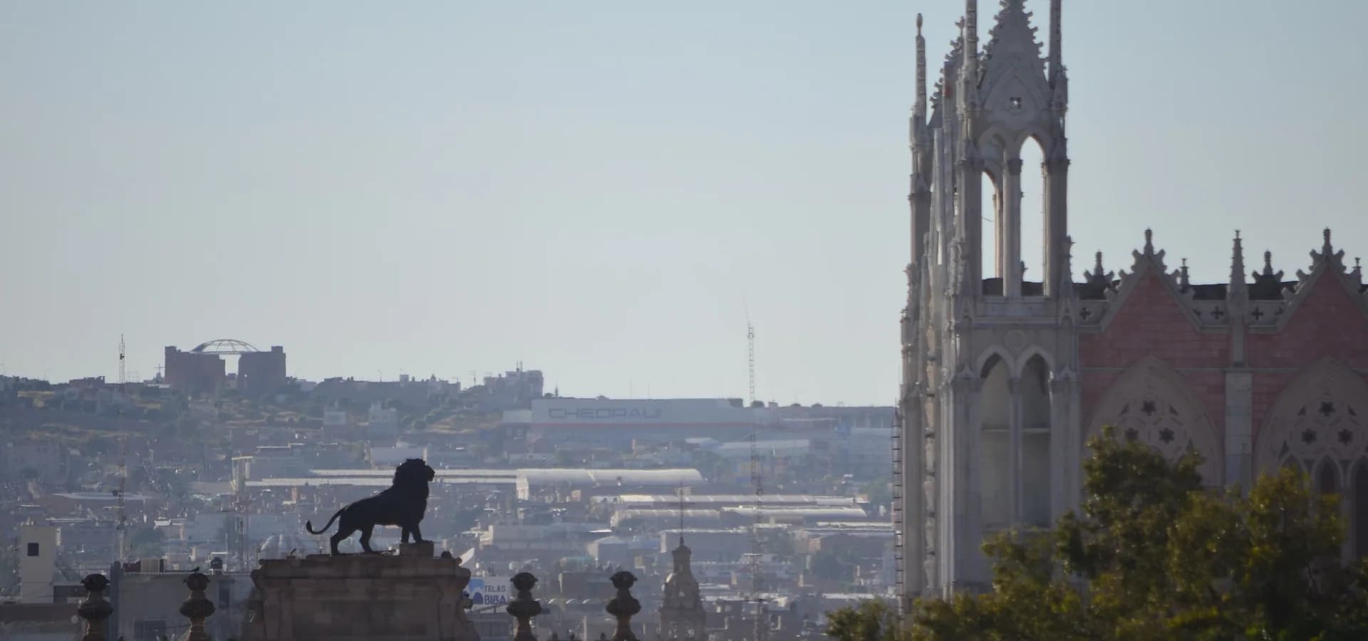 León de bronce sobre el Arco de la Calzada y las torres del Templo Expiatorio sobre los tejados de León